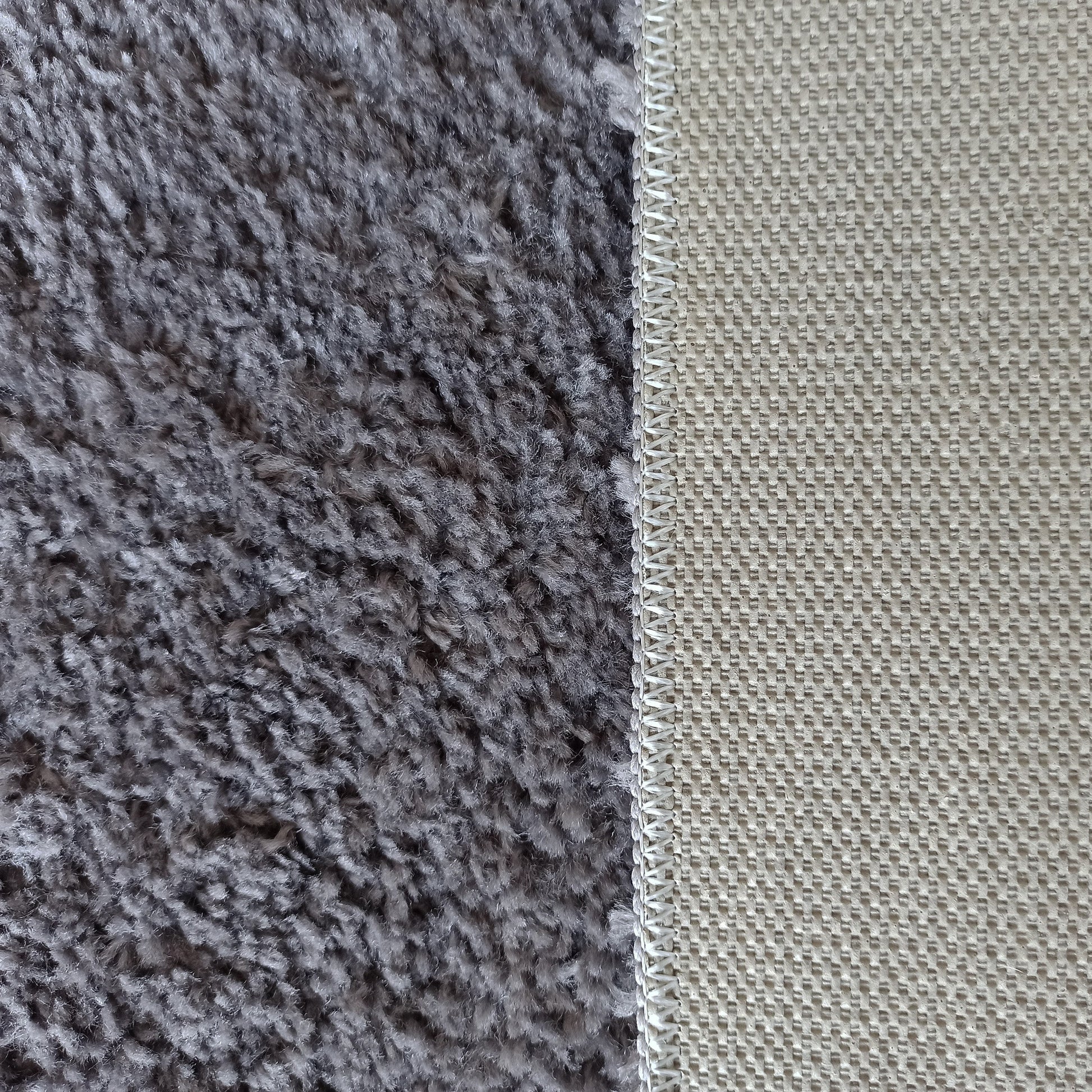 Vue rapprochée d'un tapis gris à texture velue et de son envers beige à motifs, reliés par un surjet blanc