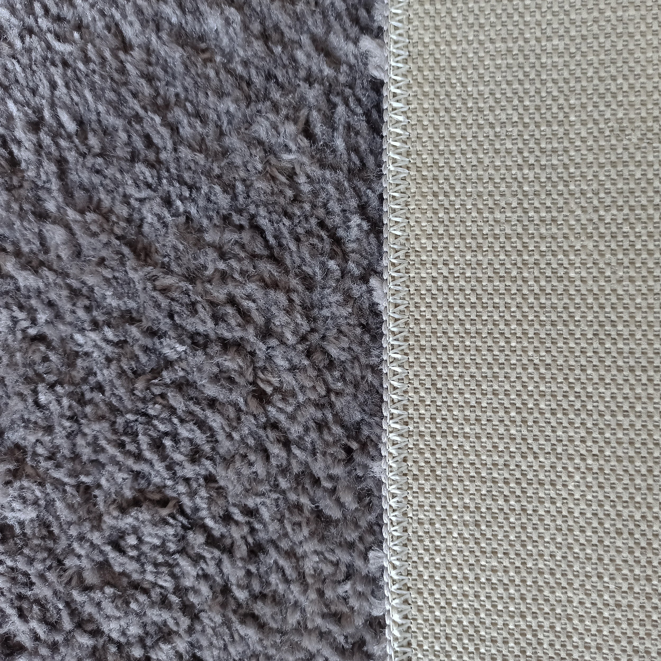 Vue rapprochée d'un tapis gris à texture velue et de son envers beige à motifs, reliés par un surjet blanc