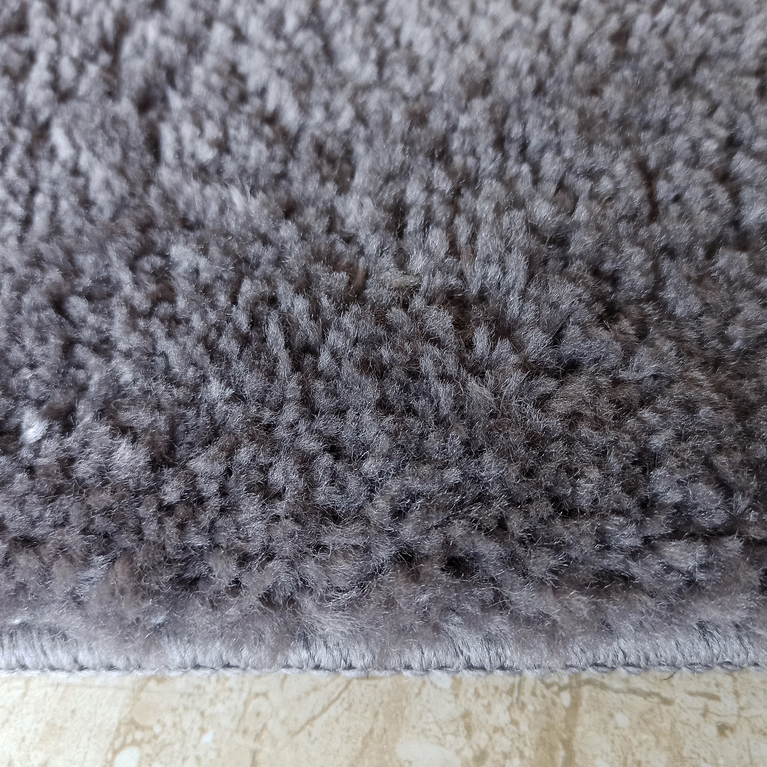 Gros plan sur un tapis gris foncé avec une texture douce et des poils longs, reposant sur un sol clair