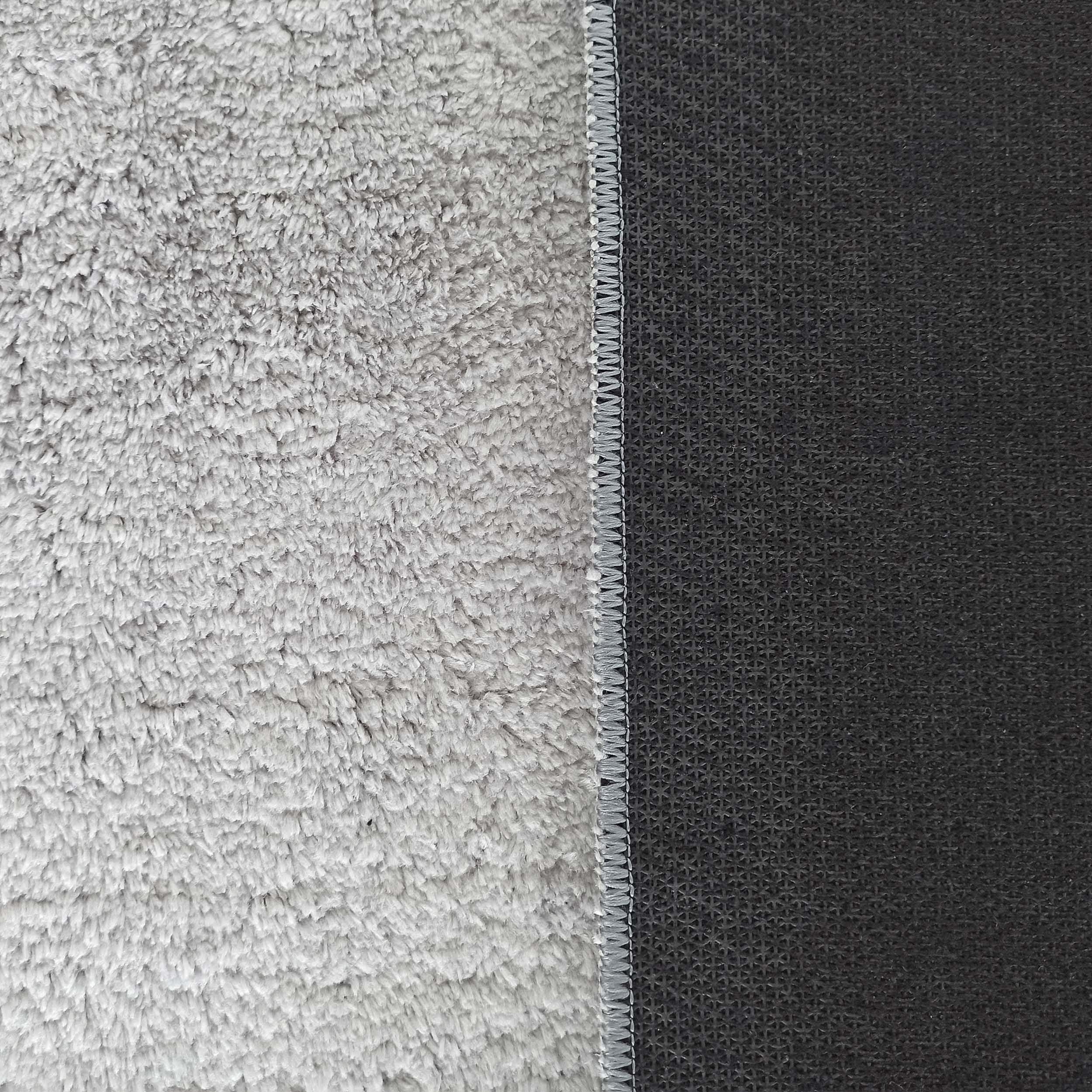 Tapis moelleux gris clair avec revers antidérapant gris foncé à motif texturé, bordé d'une couture grise