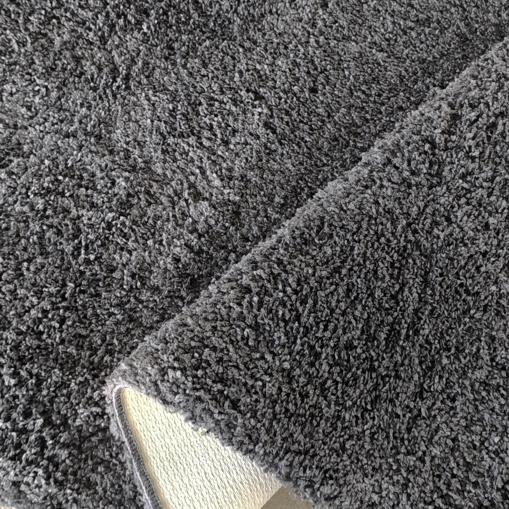 Tapis en fibres douces gris chiné, dont un coin est relevé pour montrer le dos tissé clair