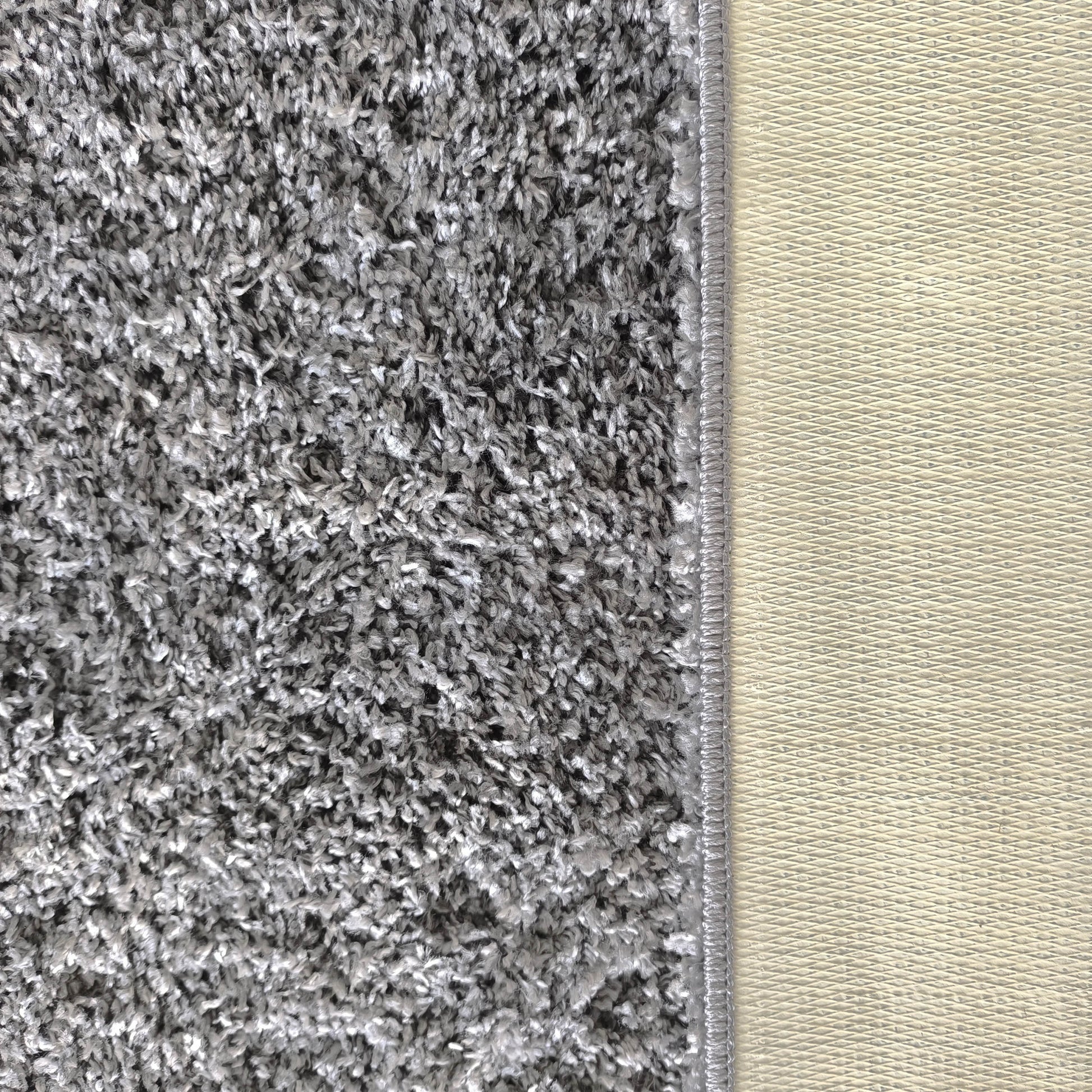 Tapis gris-blanc à poils longs et aspect shaggy, avec une bordure cousue et un envers beige clair à motif de losanges