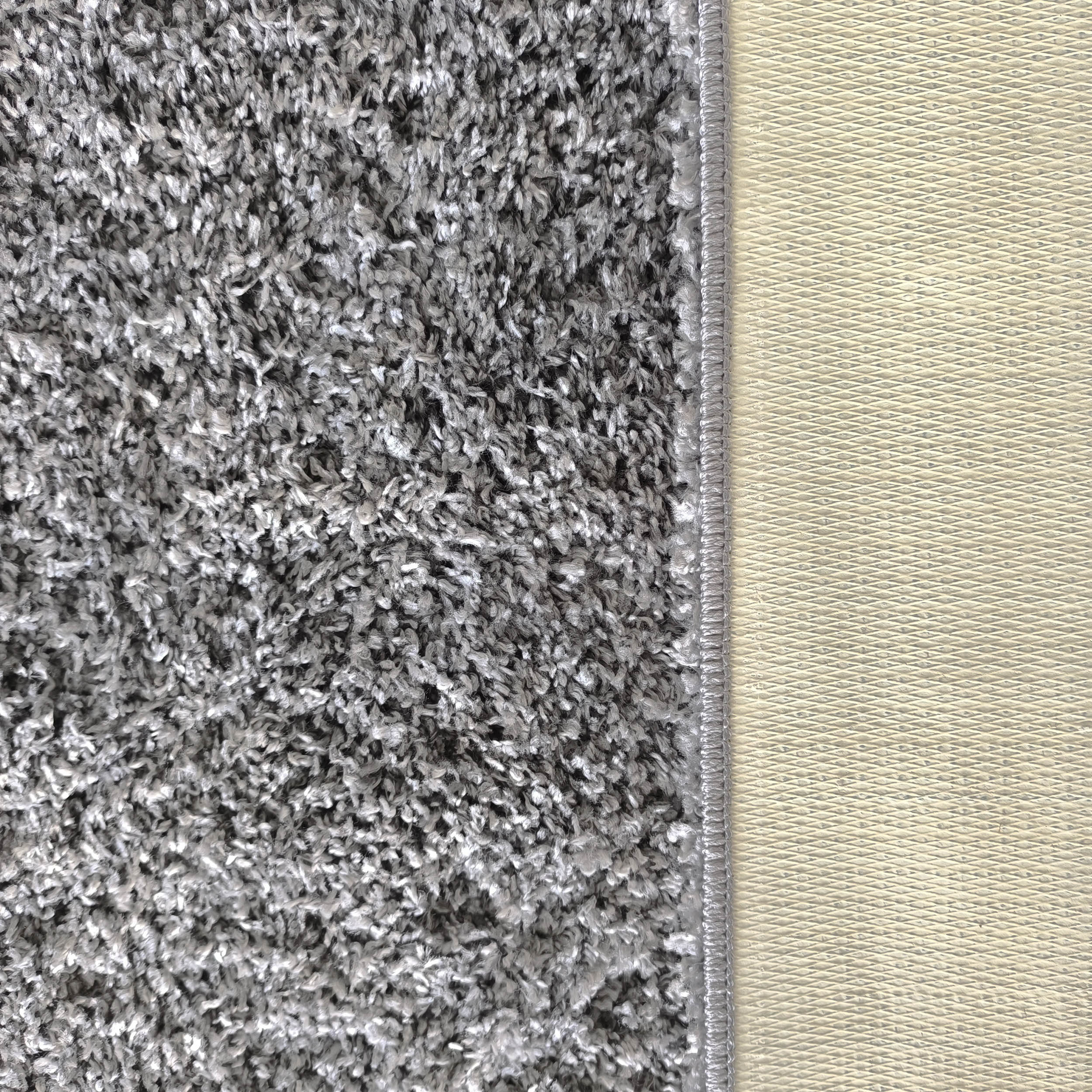 Tapis gris-blanc à poils longs et aspect shaggy, avec une bordure cousue et un envers beige clair à motif de losanges