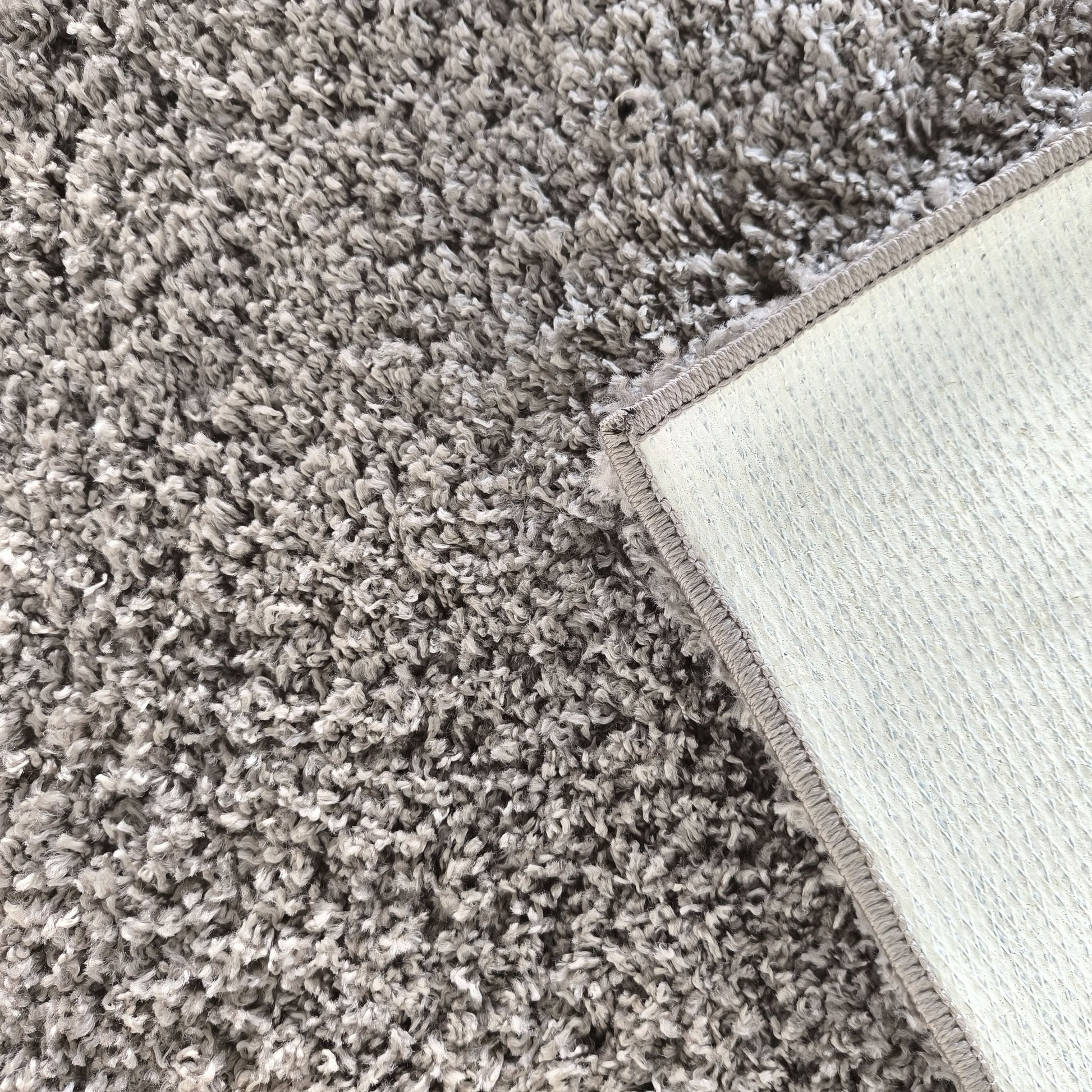 Tapis gris clair et foncé à poils longs, avec un coin relevé montrant son envers blanc texturé et son bord surpiqué