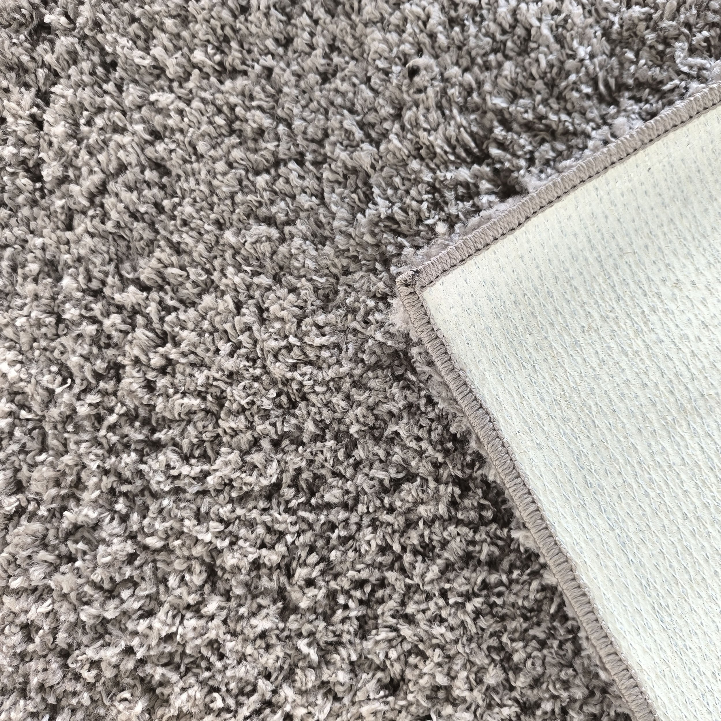 Tapis gris clair et foncé à poils longs, avec un coin relevé montrant son envers blanc texturé et son bord surpiqué