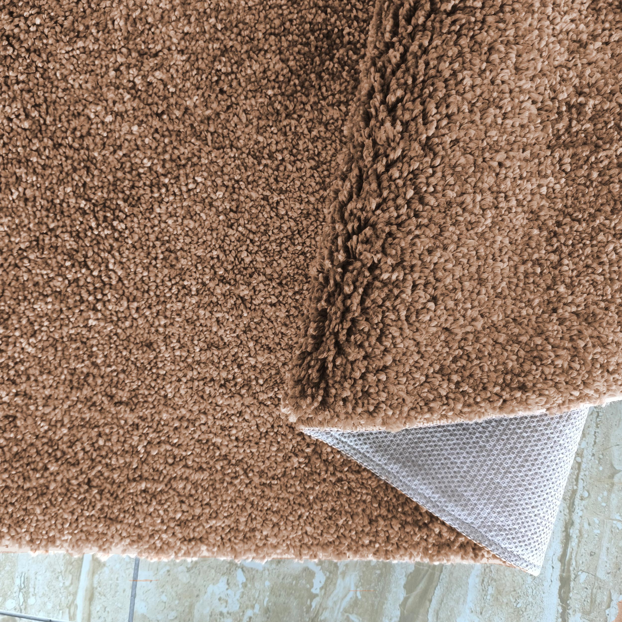 Gros plan d'un tapis marron clair à poils longs et bouclés, avec son envers gris quadrillé visible