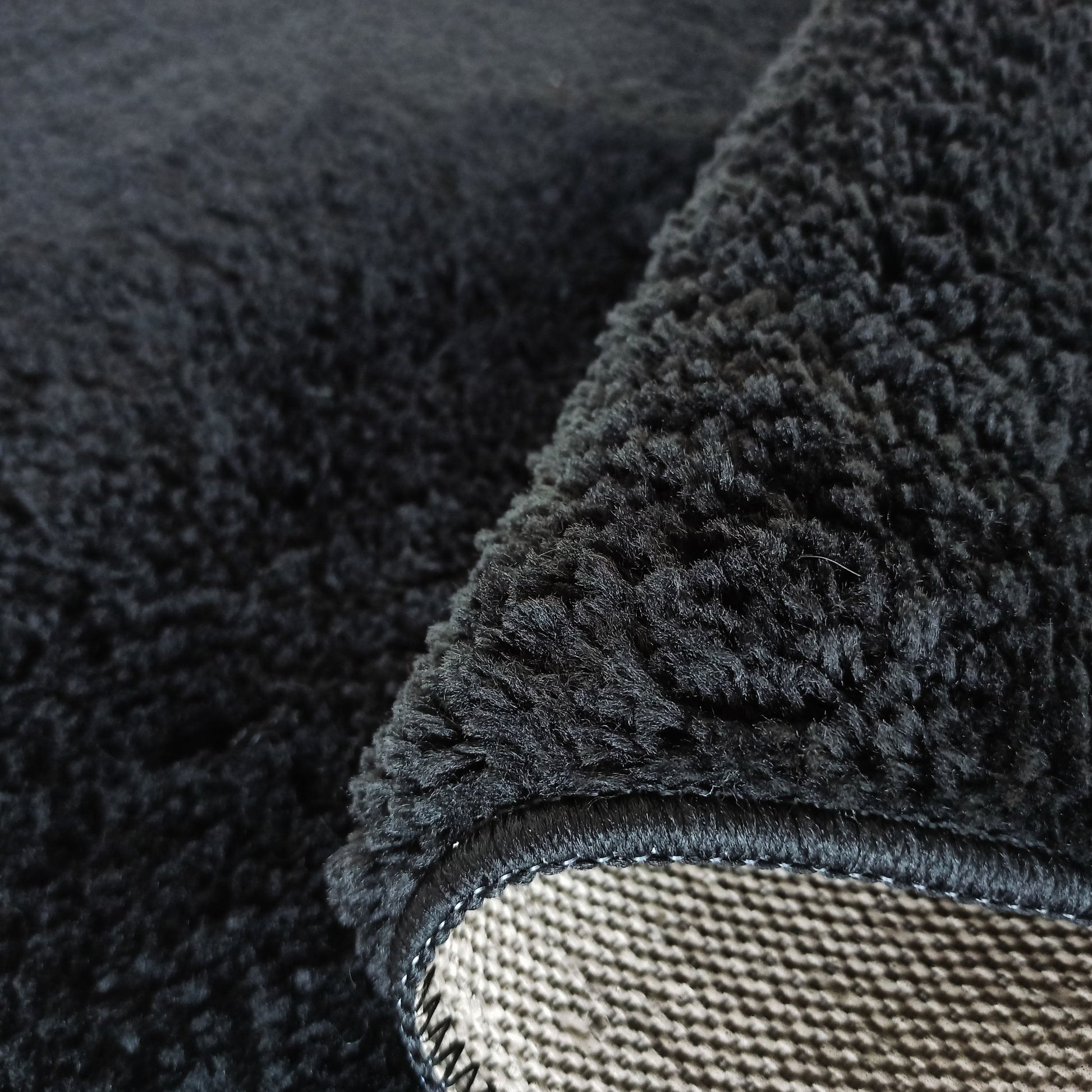 Gros plan sur un tapis noir à poils longs et doux, avec le revers clair et texturé visible sur un coin