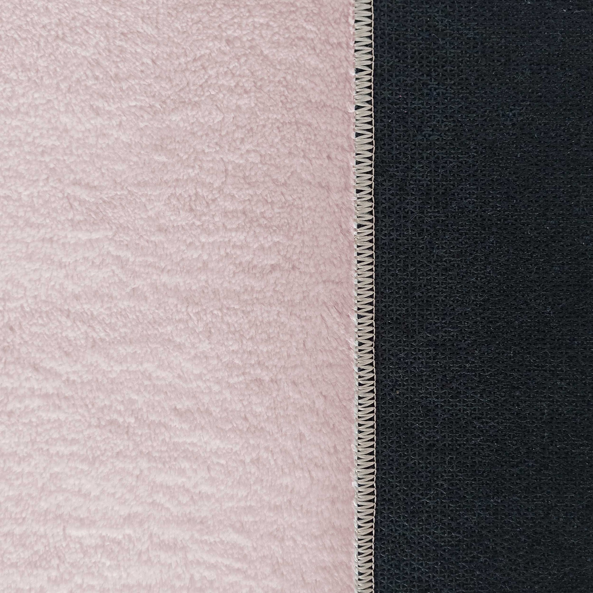 Tapis rose clair à poils longs et moelleux, avec une bordure cousue séparant la surface du revers antidérapant noir texturé