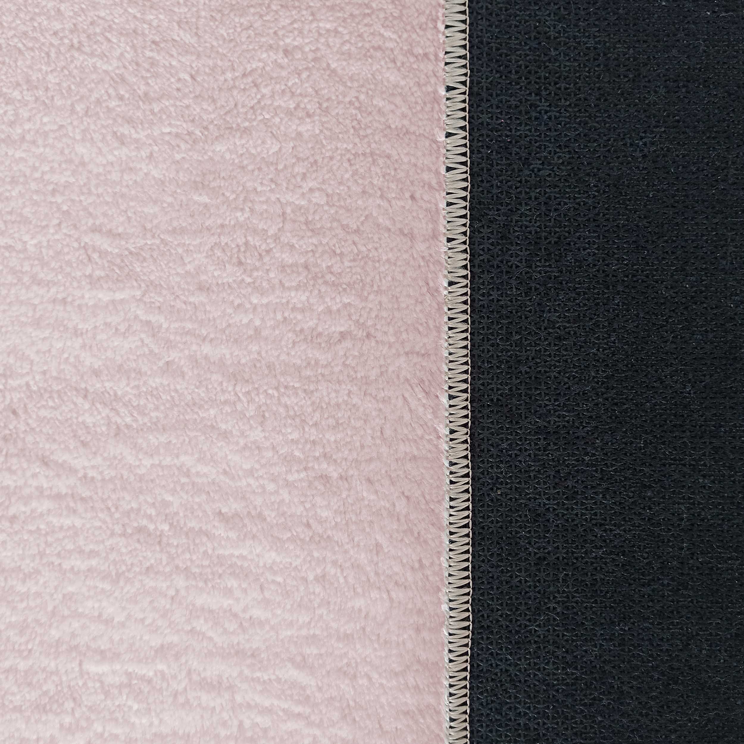 Tapis rose clair à poils longs et moelleux, avec une bordure cousue séparant la surface du revers antidérapant noir texturé