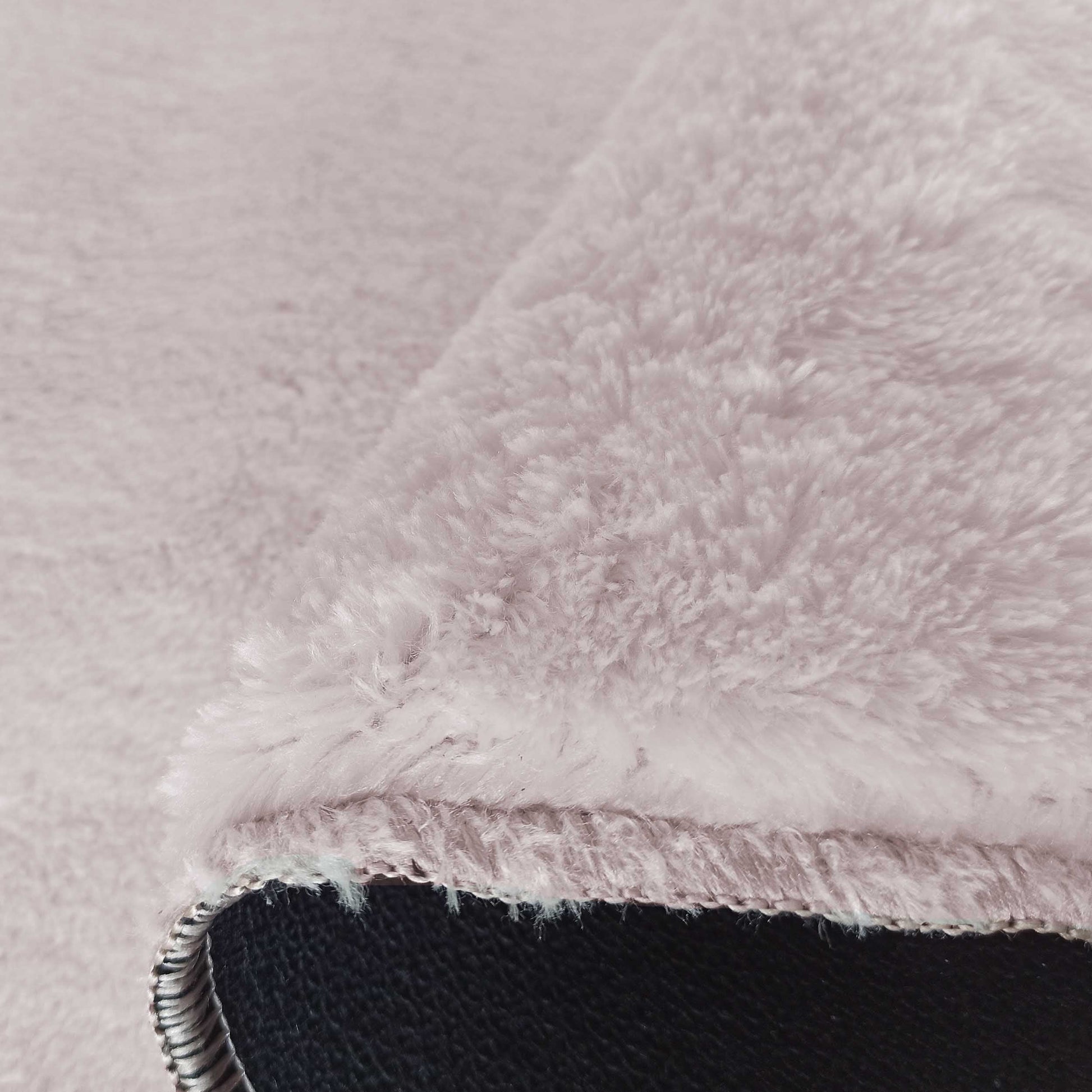 Tapis rose pâle doux et duveteux, texture rappelant la fourrure, avec un bord relevé exposant l'envers noir