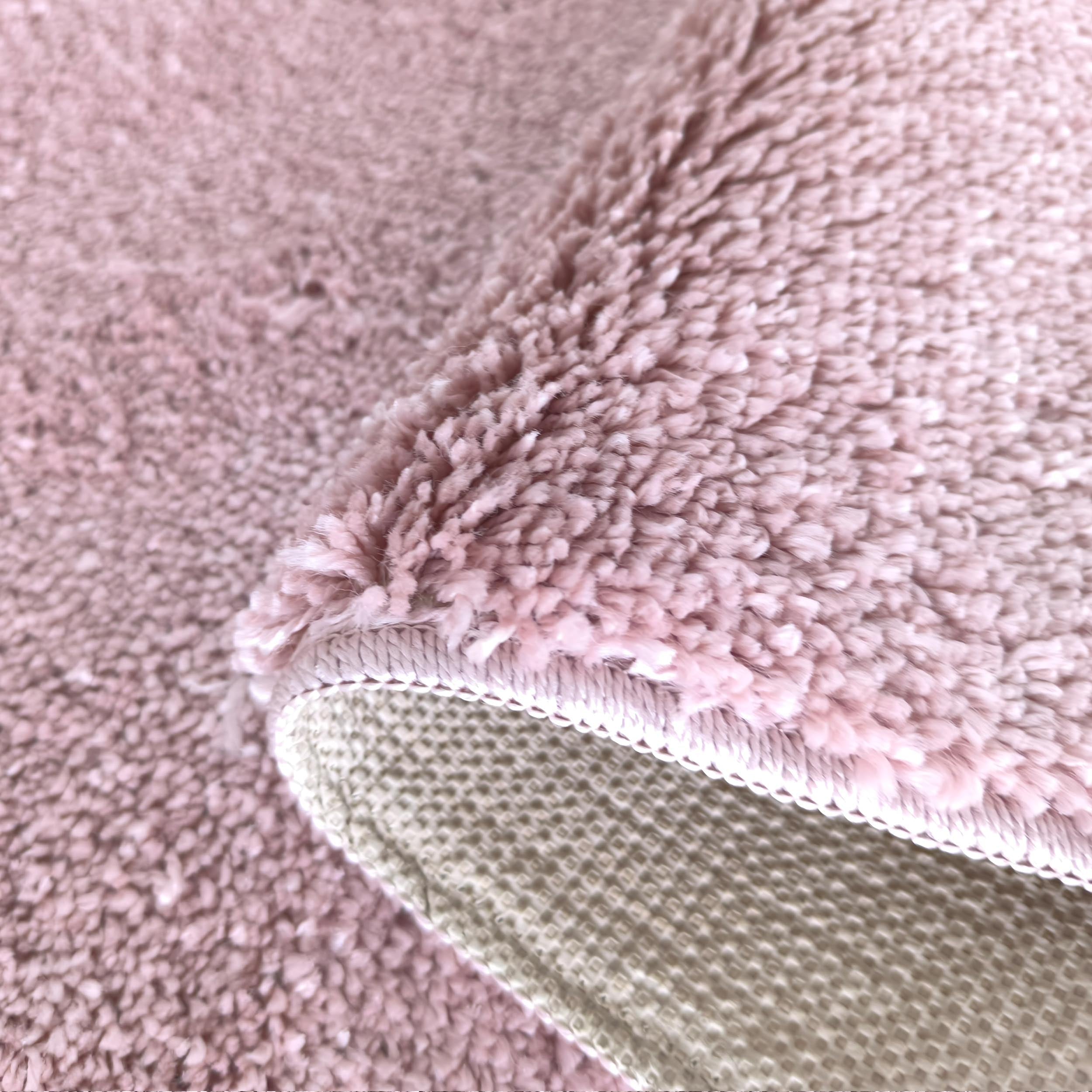 Tapis rose poudré à poils longs, montrant sa texture moelleuse et son envers tissé beige clair et quadrillé