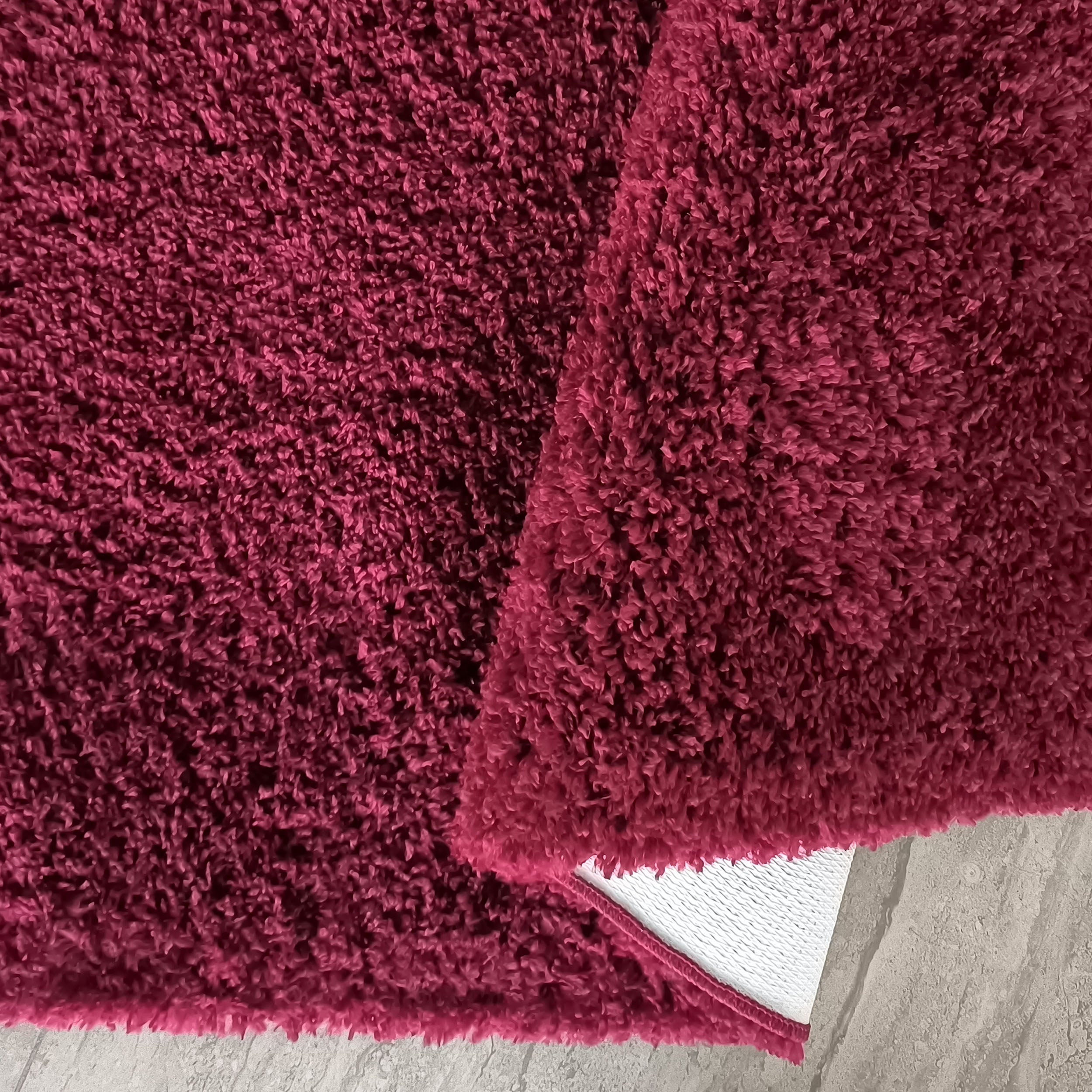Tapis rouge magenta à poils longs et épais, une section repliée révèle son envers blanc sur un sol clair