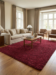 Tapis rectangulaire rouge bordeaux à poils longs et texture épaisse, posé sur un parquet clair dans un salon lumineux