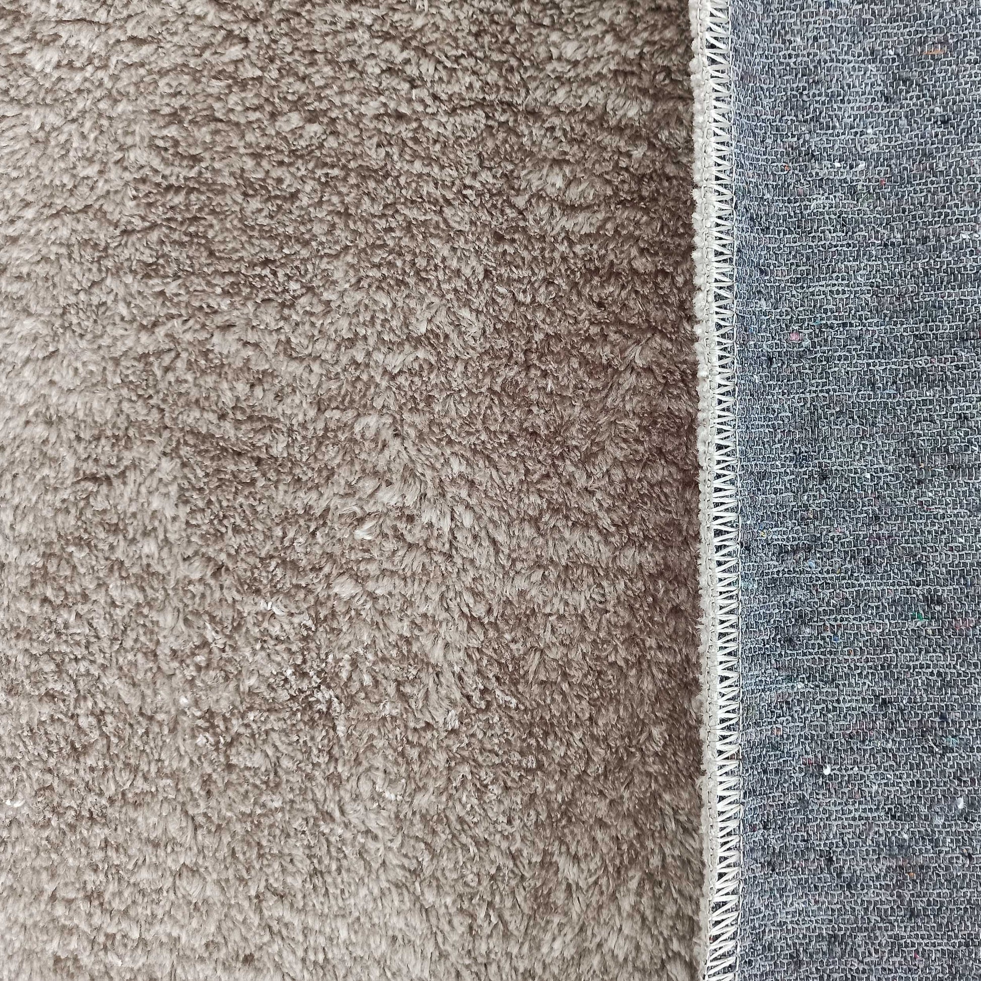 Tapis moelleux beige à poils longs montrant son envers tissé gris et une bordure surjetée blanche