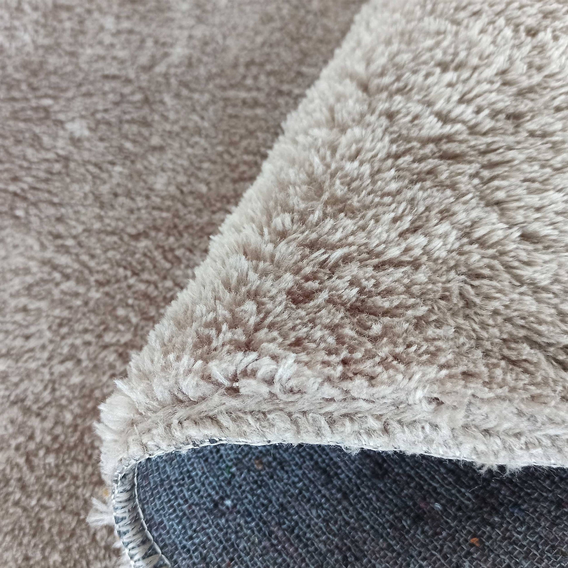 Gros plan sur un tapis beige à poils longs et doux, replié pour montrer son envers gris foncé tissé