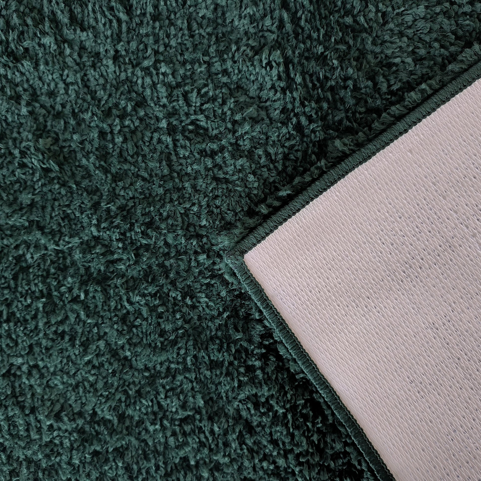 Gros plan sur un tapis shaggy vert foncé, un coin replié dévoile son envers gris clair texturé et sa bordure cousue