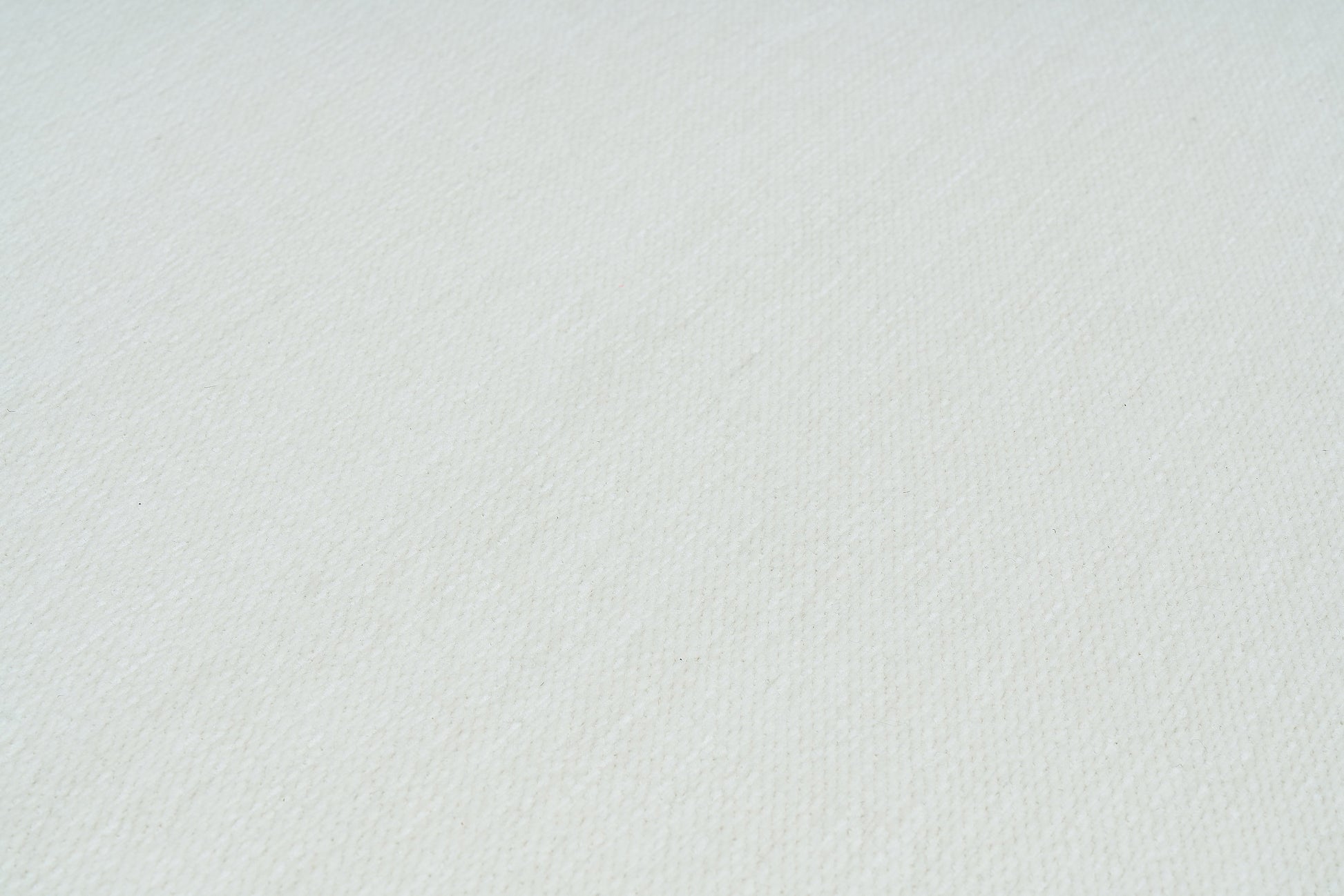 Gros plan sur la texture d'un tapis blanc uni, révélant les fibres et leur tissage serré, idéal pour un intérieur lumineux.