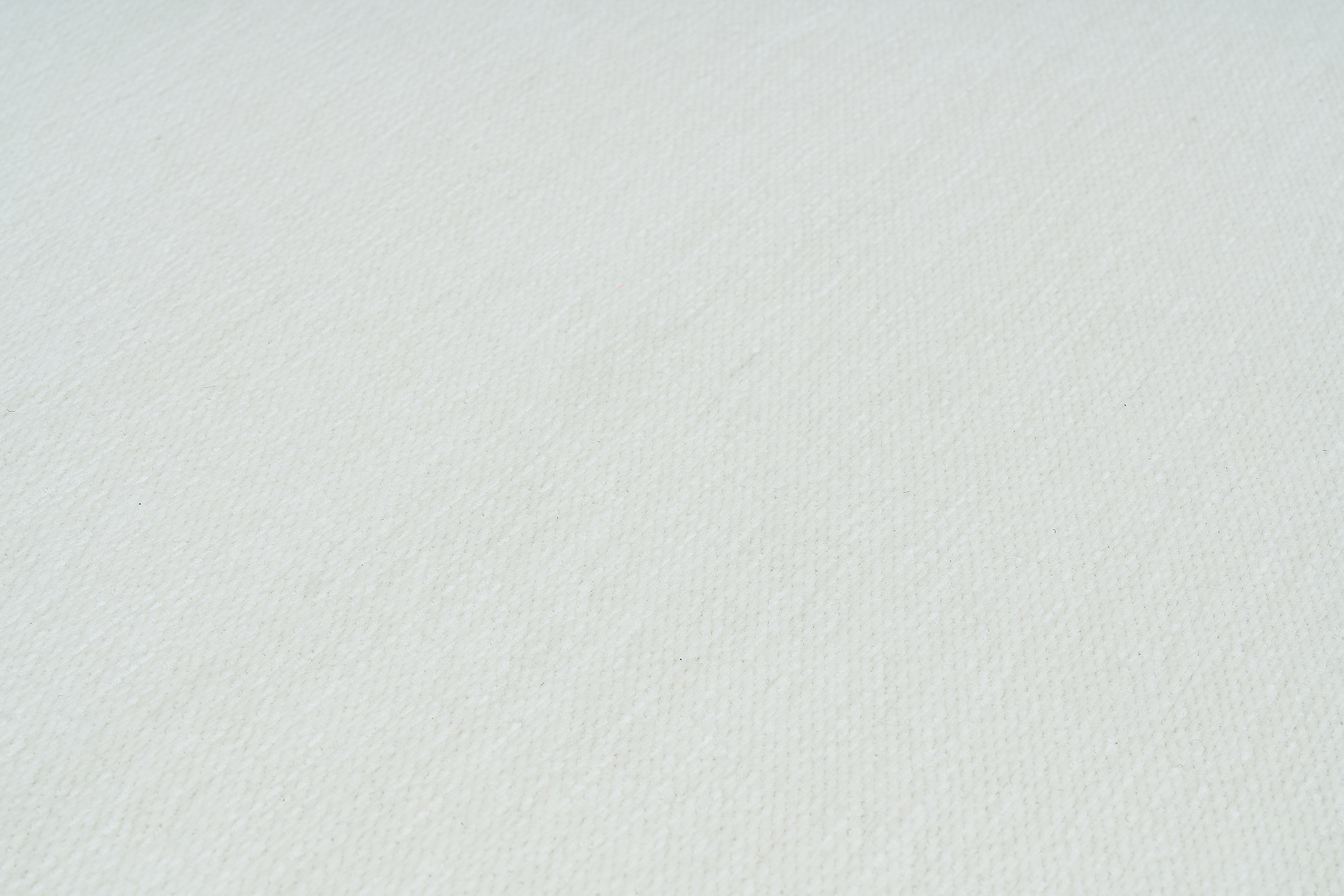 Gros plan sur la texture d'un tapis blanc uni, révélant les fibres et leur tissage serré, idéal pour un intérieur lumineux.