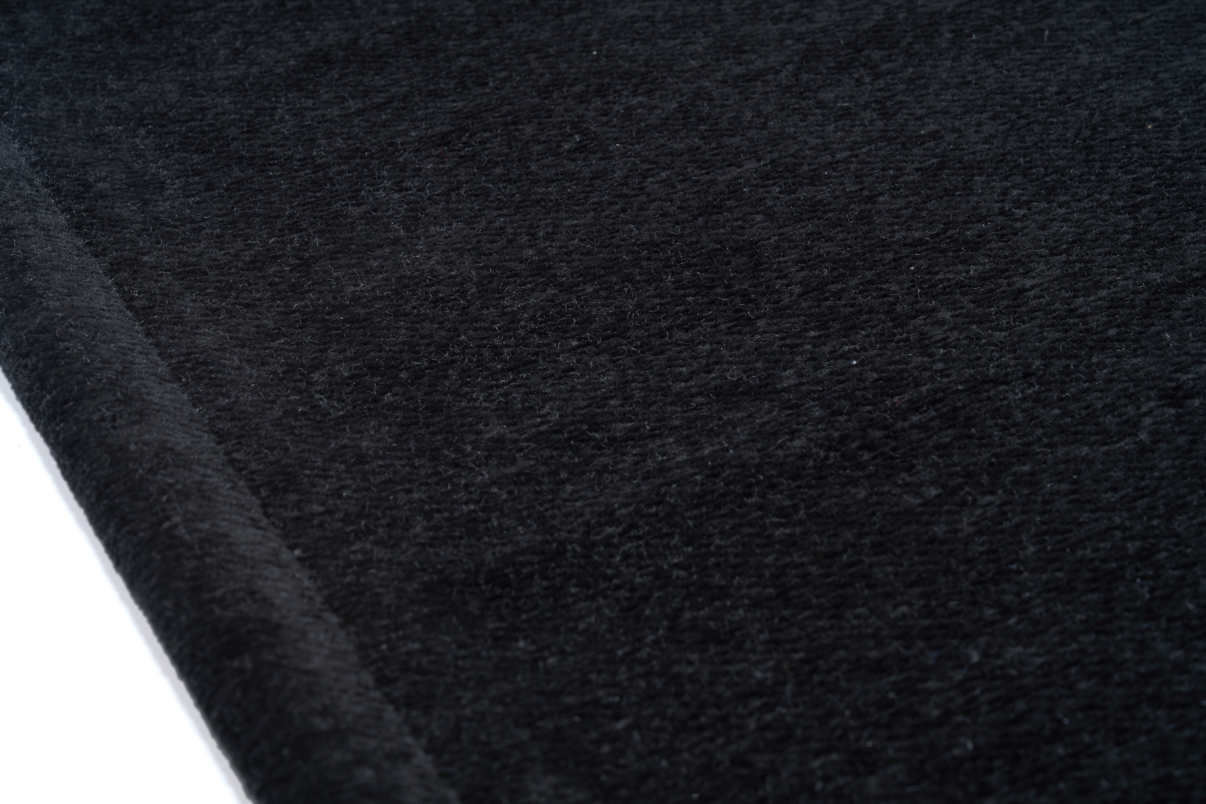 Gros plan sur la texture d'un tapis noir uni, révélant des fibres douces et denses, parfaites pour le confort et le style.