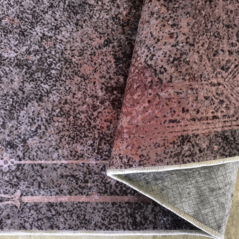 Tapis à motifs abstraits mouchetés de gris, noir, et des nuances de rose foncé, avec un envers texturé visible sur le côté