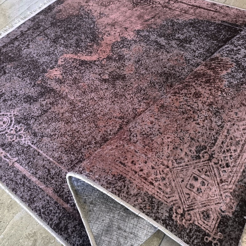 Tapis texturé aux teintes délavées de marron foncé et de rose, avec des motifs ornementaux, partiellement roulé