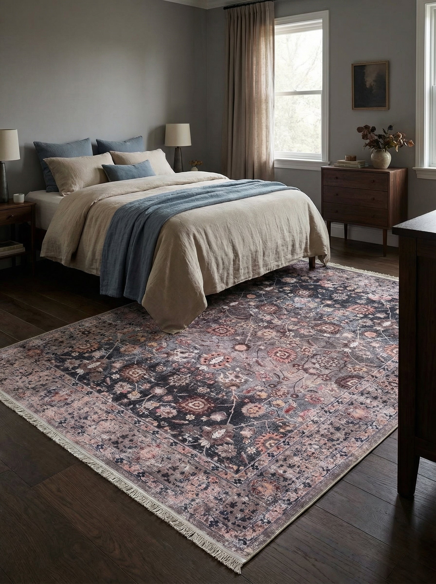Tapis rectangulaire esprit persan avec motifs floraux et géométriques dans des tons noir, rose, beige et rouille, aux bordures frangées, dans une chambre