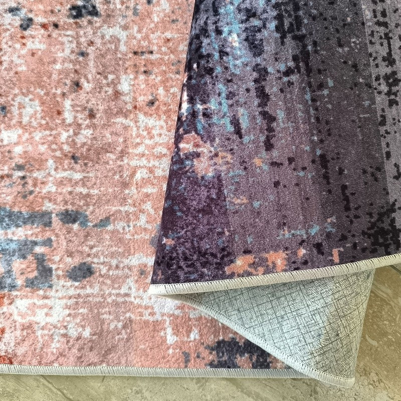 Tapis doux aux motifs abstraits et délavés rose saumon, violet et bleu canard, son revers gris texturé est visible