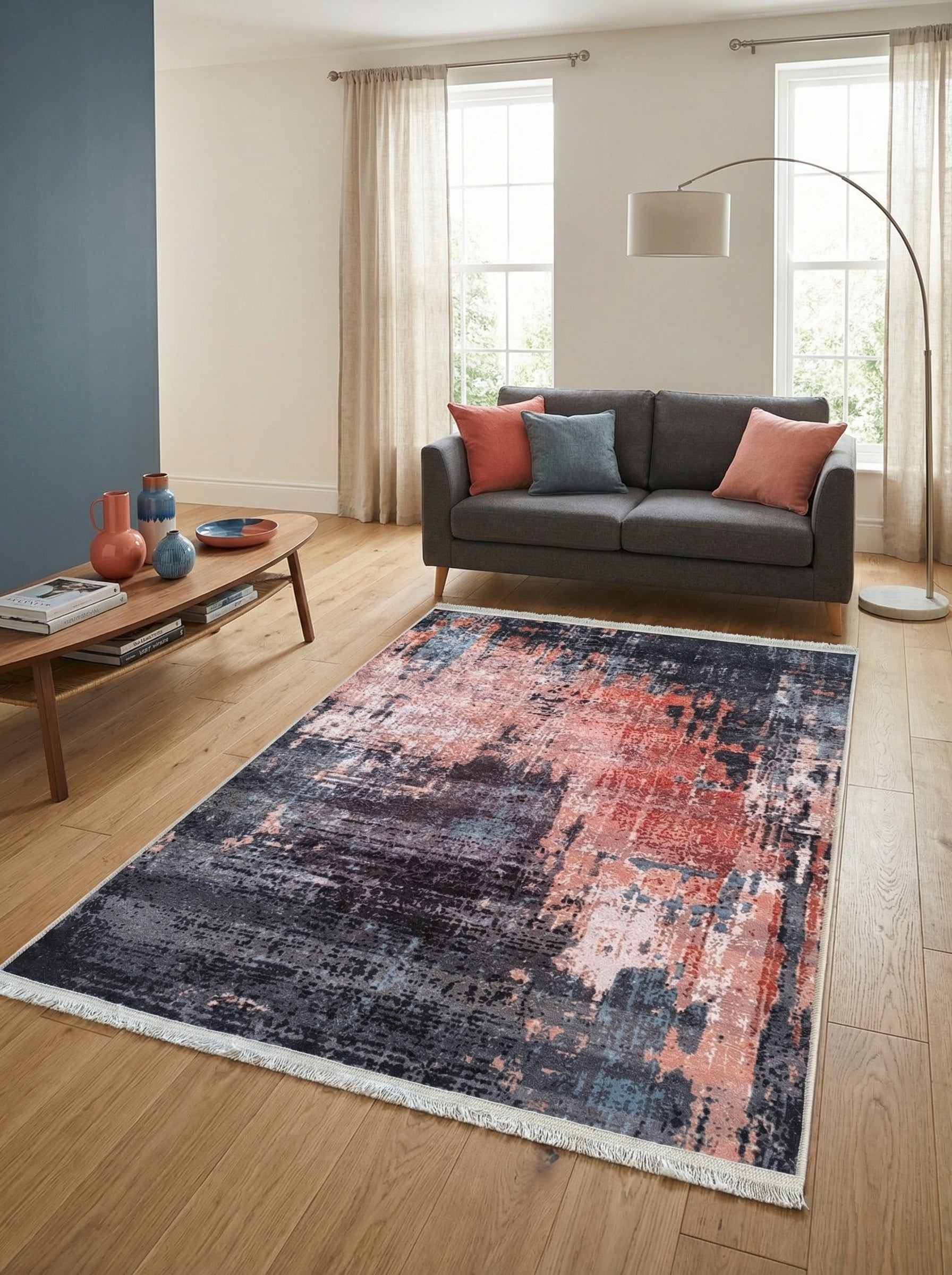 Tapis rectangulaire à motif abstrait gris foncé, rouille et bleu clair, avec franges, posé sur un parquet clair dans un salon moderne