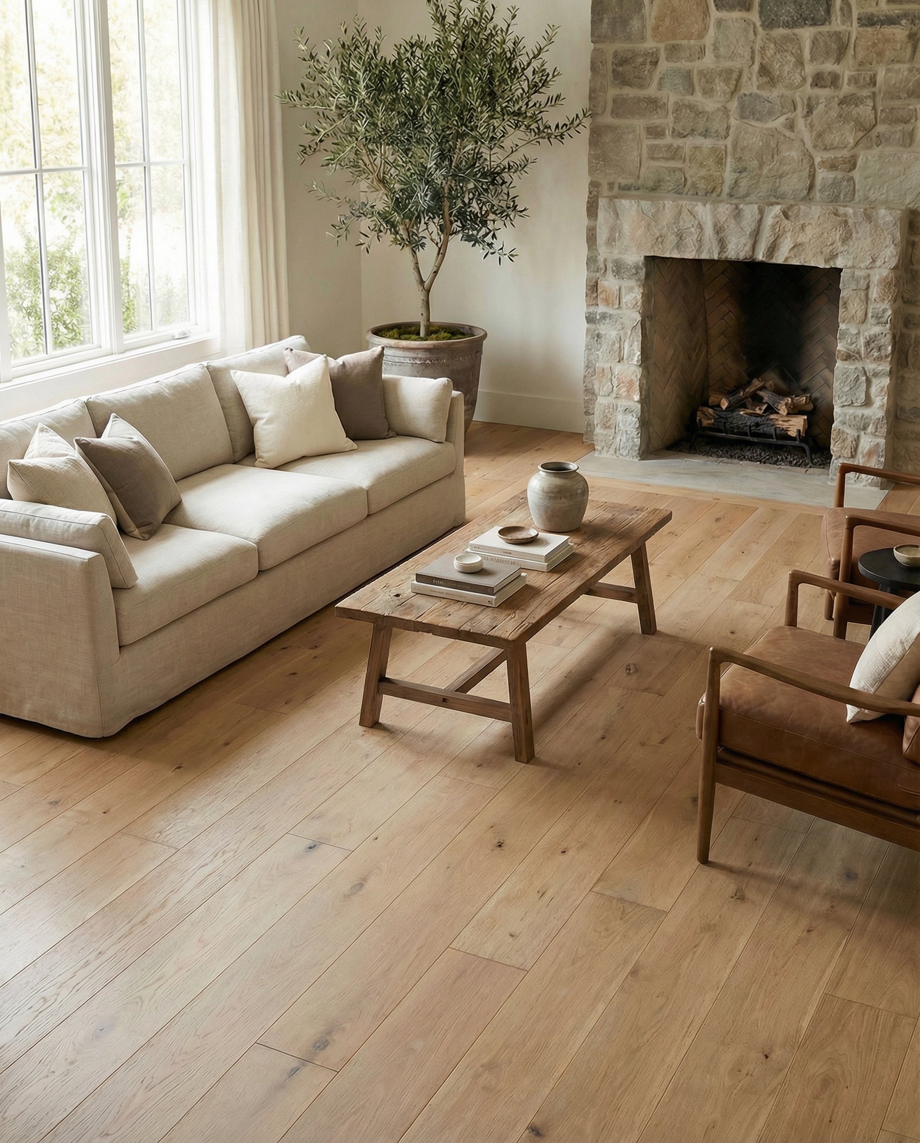 Pièce avec plancher en bois clair, canapé beige, fauteuils en cuir, cheminée en pierre, ambiance chaleureuse