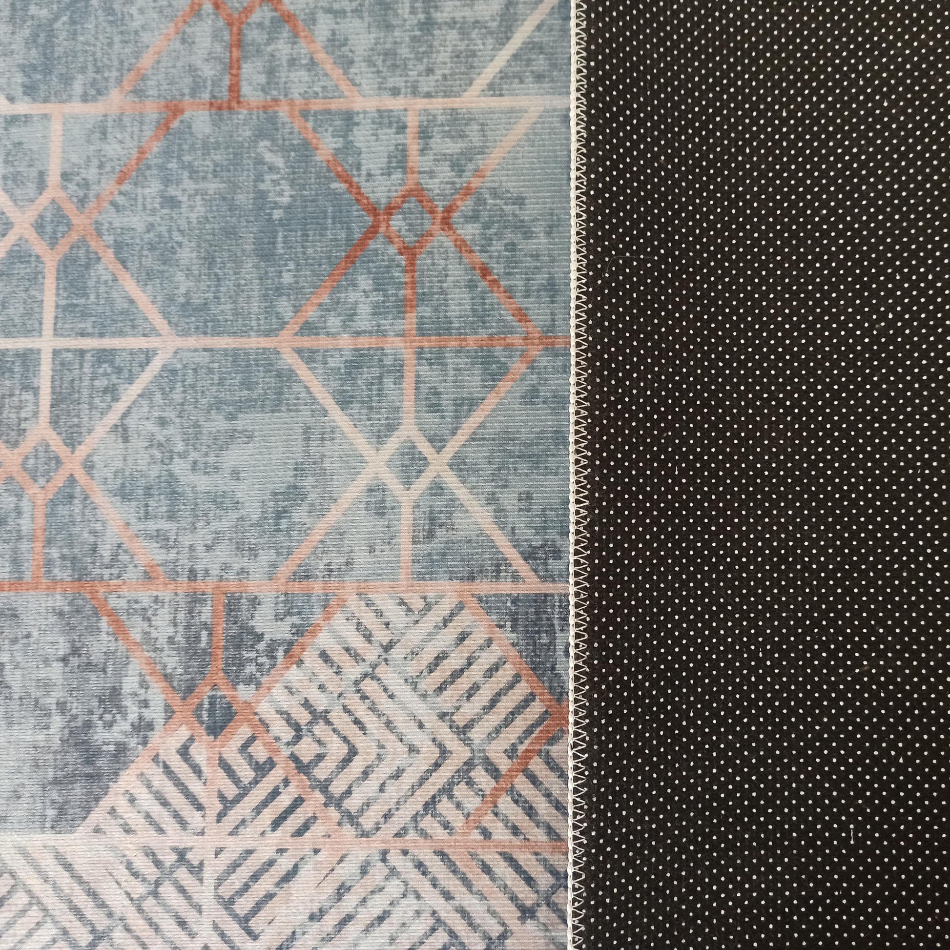 Tapis double-face : dessus bleu-gris à motifs géométriques pêche, dessous antidérapant noir à petits pois blancs, reliés par une couture