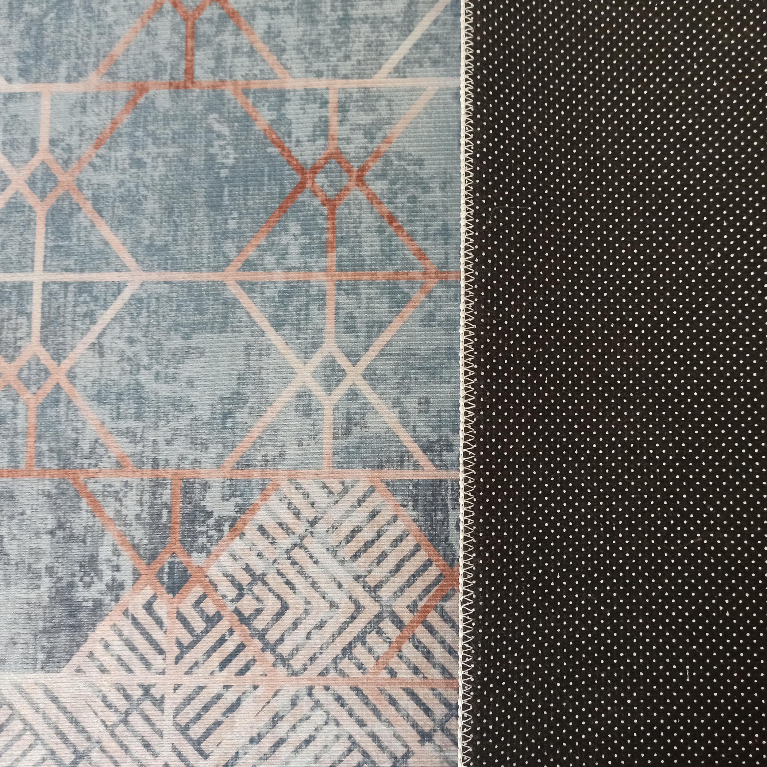 Tapis double-face : dessus bleu-gris à motifs géométriques pêche, dessous antidérapant noir à petits pois blancs, reliés par une couture