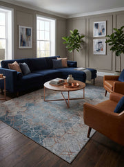 Tapis rectangulaire aux motifs géométriques bleus, gris clairs et cuivrés, créant un effet usé dans un salon contemporain