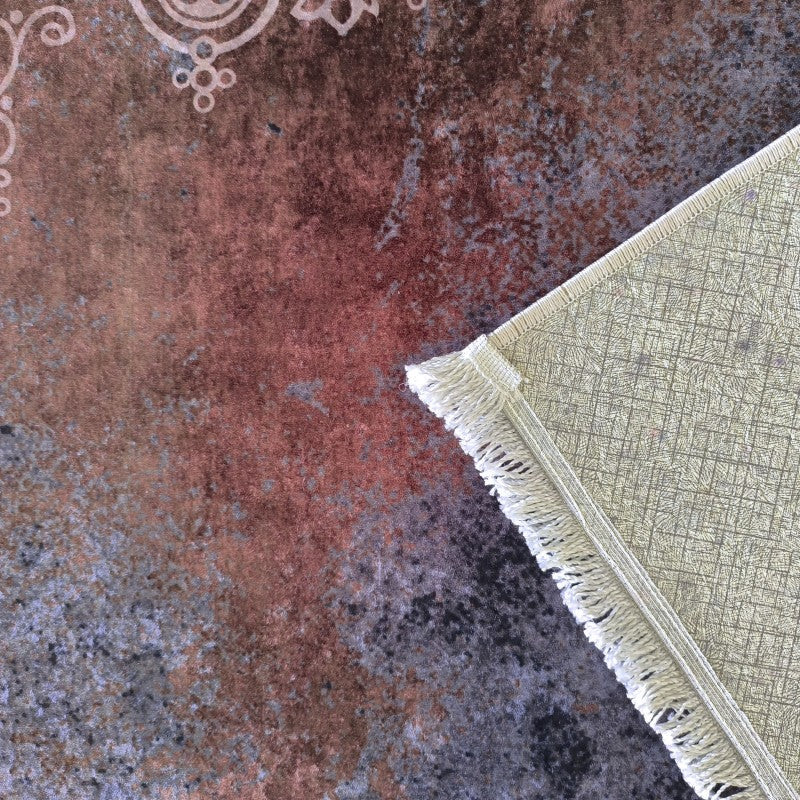 Tapis à surface abstraite marron-rouge et grise, avec des motifs ornementaux clairs. Son coin replié révèle l'envers clair quadrillé et des franges