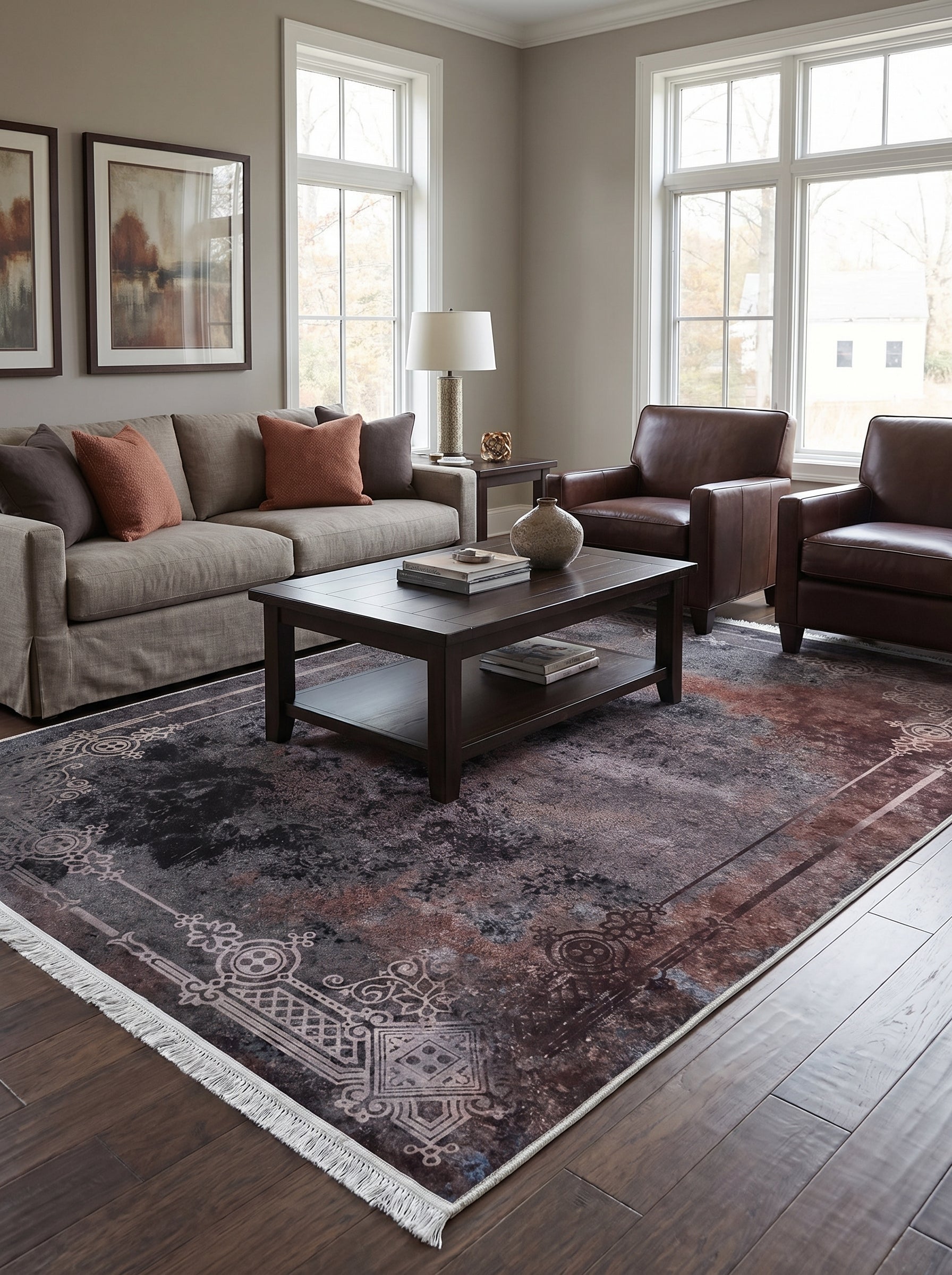 Tapis rectangulaire aux motifs ornementaux gris clair sur fond abstrait marron rouille et gris anthracite avec franges, dans un salon