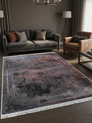 Grand tapis rectangulaire aux teintes sombres gris-anthracite et rouille, motifs floraux stylisés clairs en bordure et franges, dans un salon