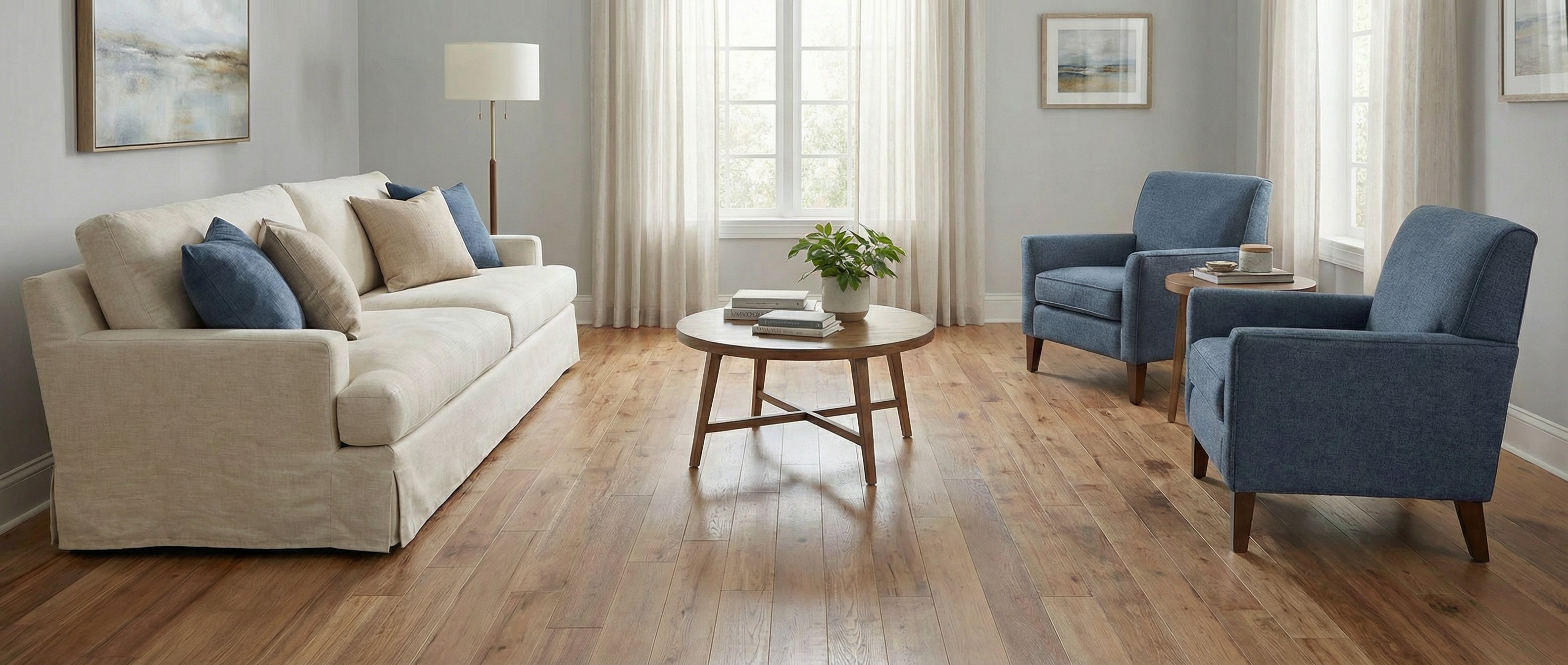 Pièce lumineuse avec canapé, fauteuils bleus, table ronde en bois. Sol en bois clair, espace vide pour tapis rectangulaire