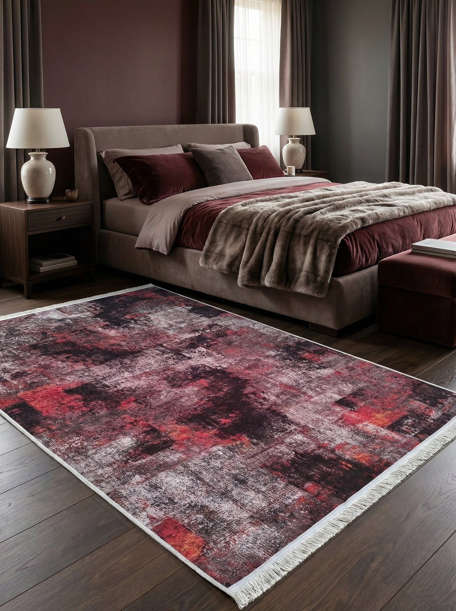 Tapis rectangulaire aux motifs abstraits et délavés en teintes de bordeaux, rouge, noir et gris clair, avec franges blanches, posé sur un parquet sombre dans une chambre cosy