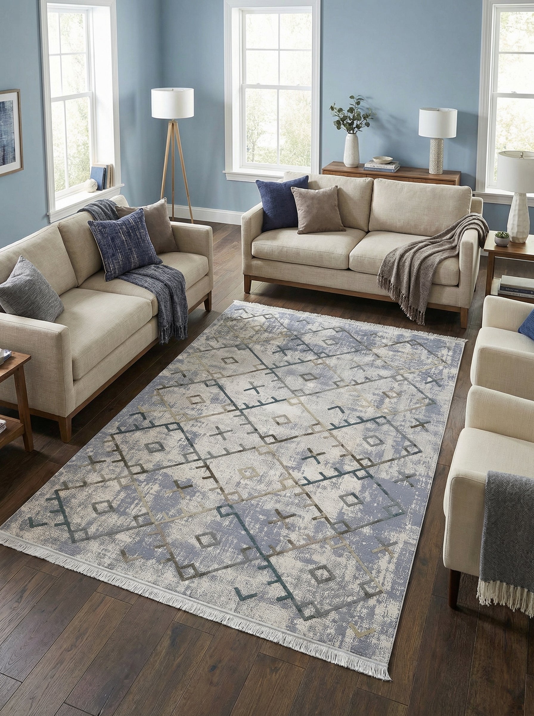 Tapis rectangulaire aux motifs géométriques abstraits gris clair, bleu-gris et taupe sur fond texturé, avec franges, dans un salon contemporain