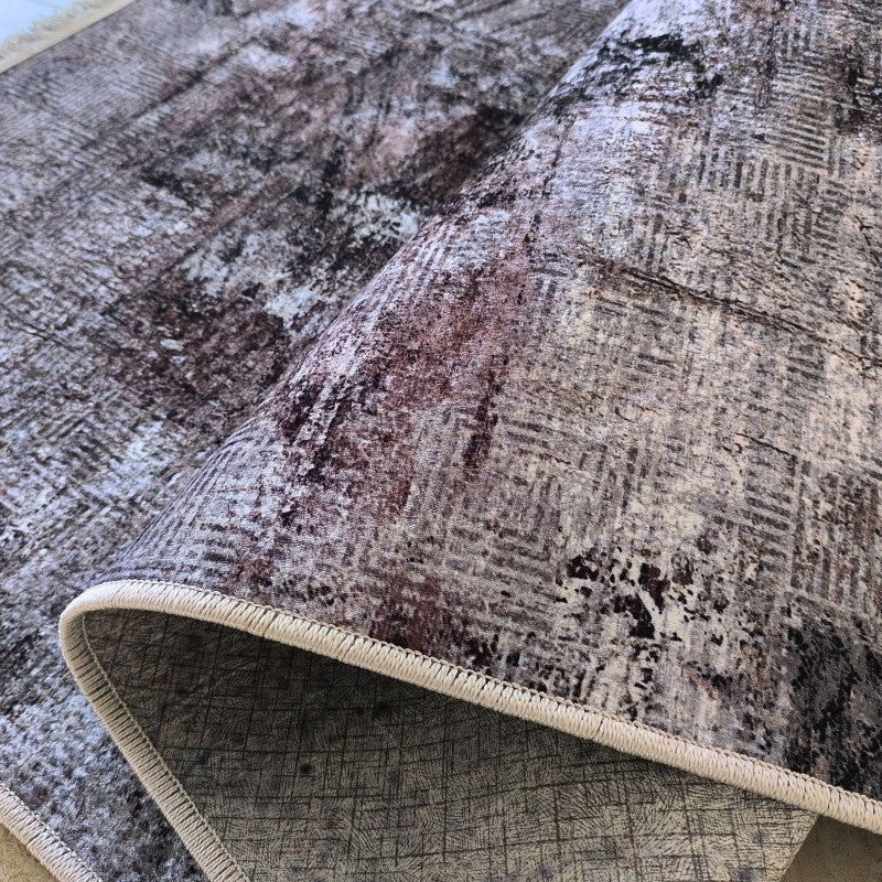Tapis pelucheux avec un motif abstrait de gris, blanc, brun-rouge et noir, donnant une impression usée. Il est partiellement enroulé