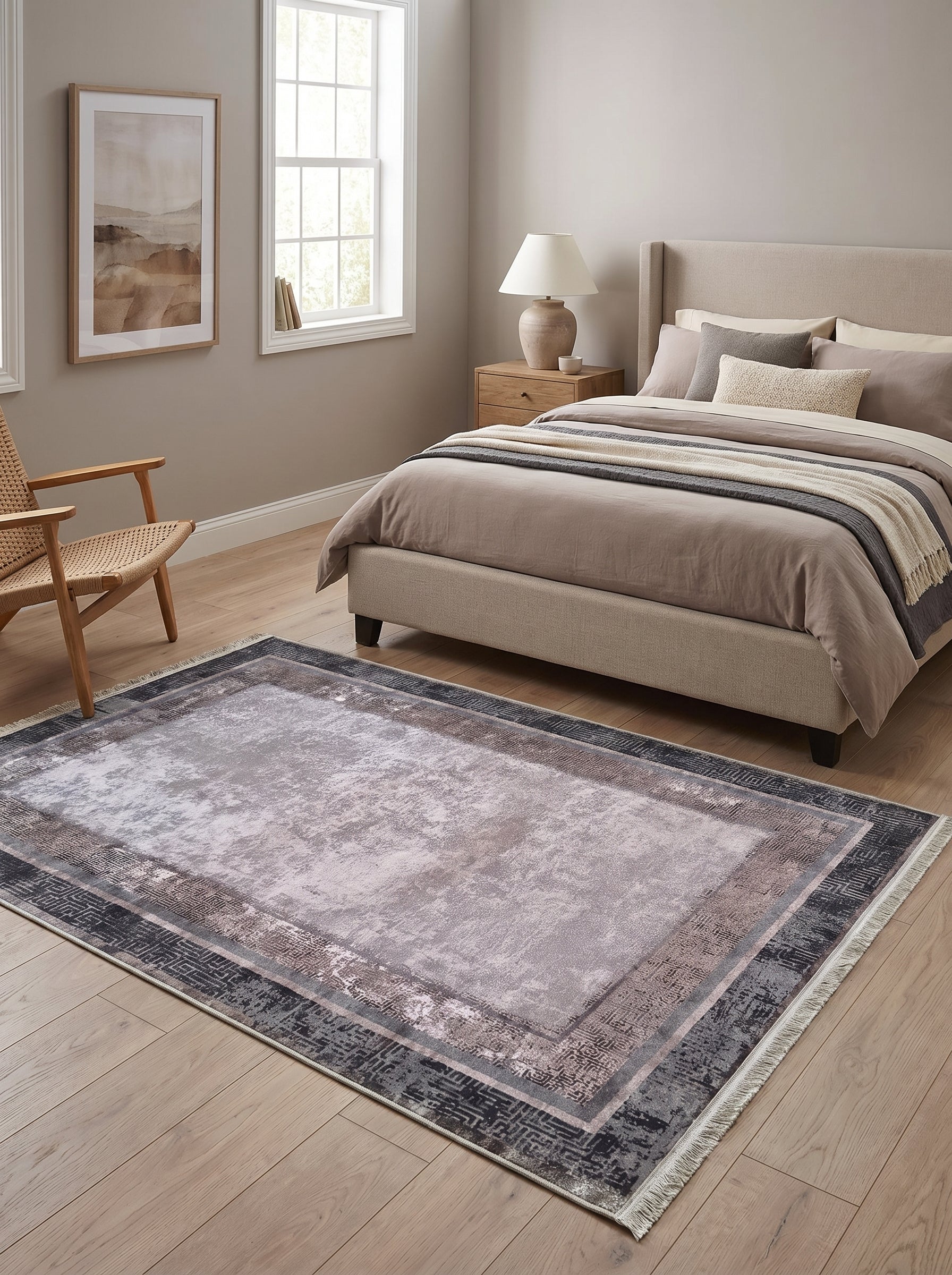 Tapis rectangulaire gris clair, rose poudré et anthracite avec un motif central abstrait délavé et une bordure ornementale, posé dans une chambre