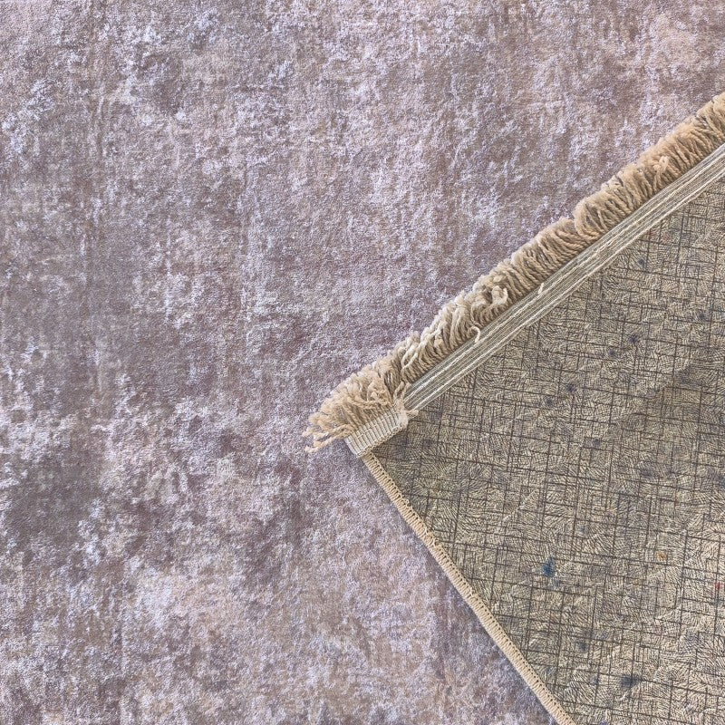 Tapis à la texture mouchetée beige et grise, un coin relevé dévoile le dos quadrillé et les franges