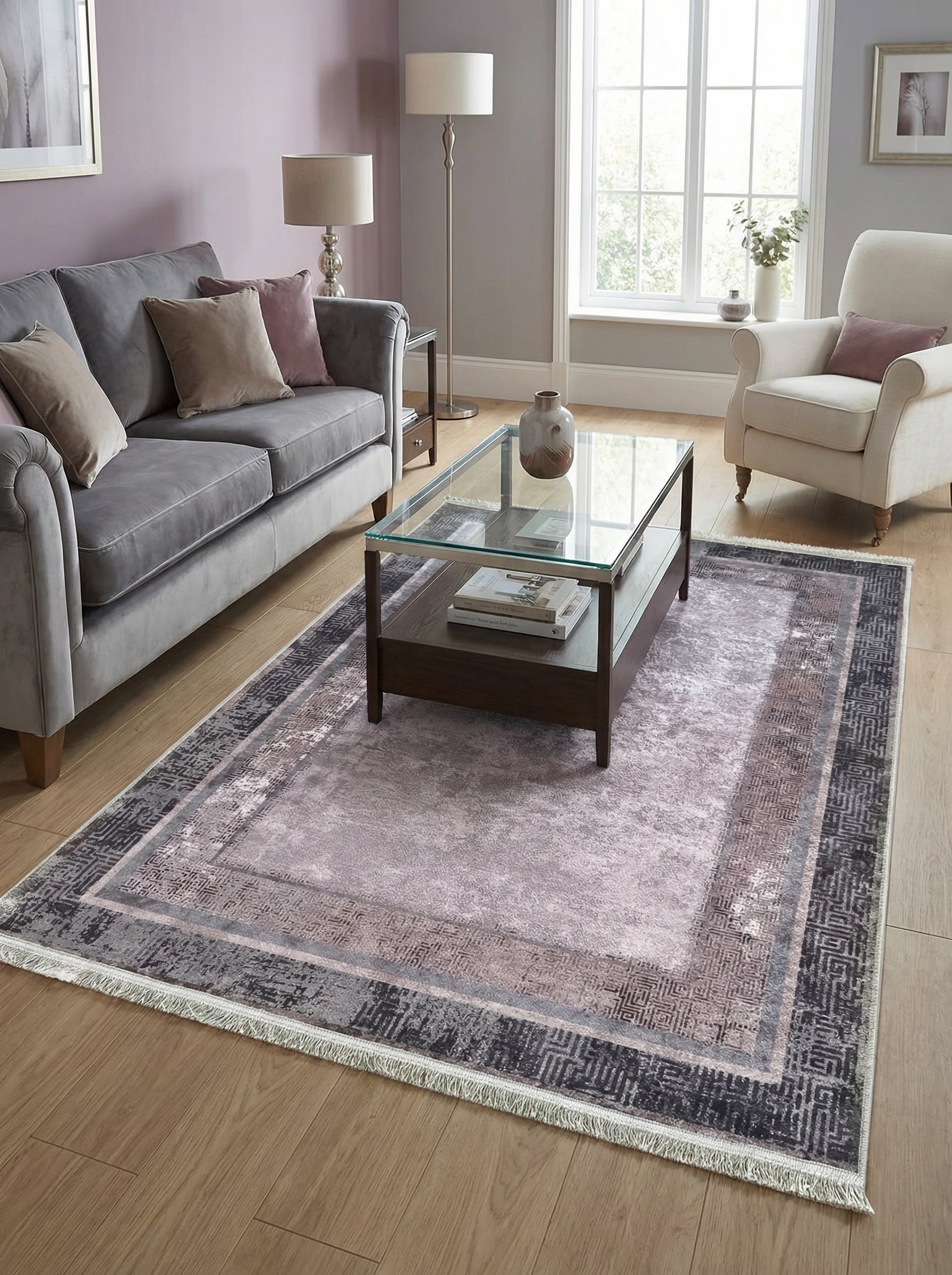 Tapis rectangulaire à franges, au centre lilas pâle texturé et bordures géométriques grises, anthracite et rose-brun, dans un salon