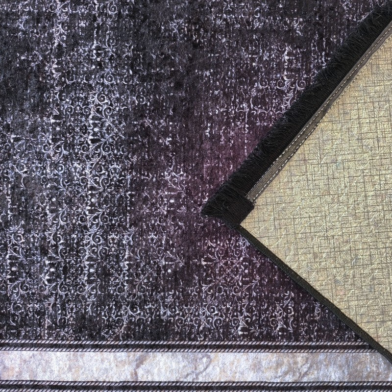 Tapis sombre aux motifs ornementaux blancs sur fond dégradé gris violacé, avec une bordure striée et une sous-face beige quadrillée et frangée