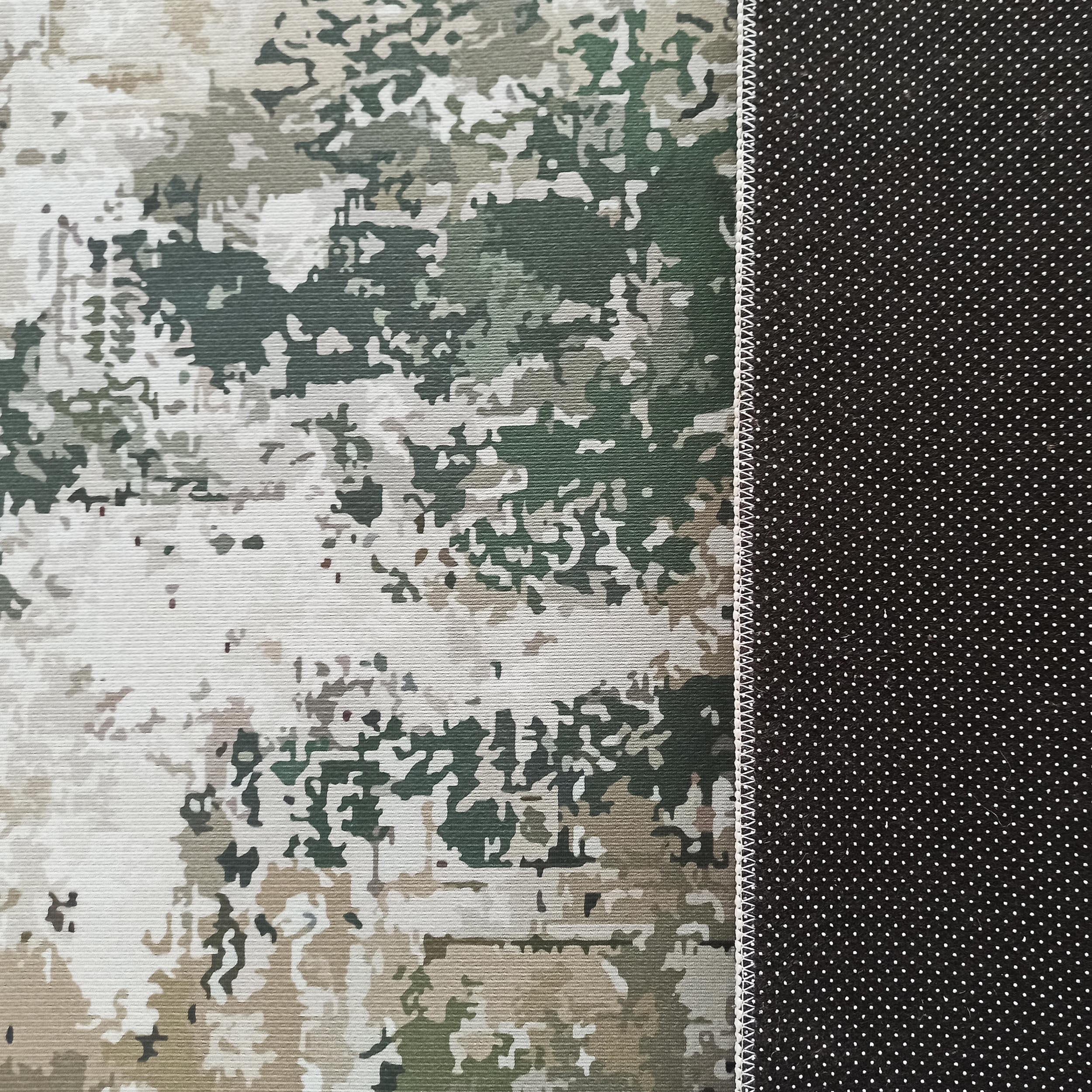 Tapis au motif camouflage vert, beige, gris et blanc, bordé d'une couture zigzag blanche, avec un dessous noir à picots