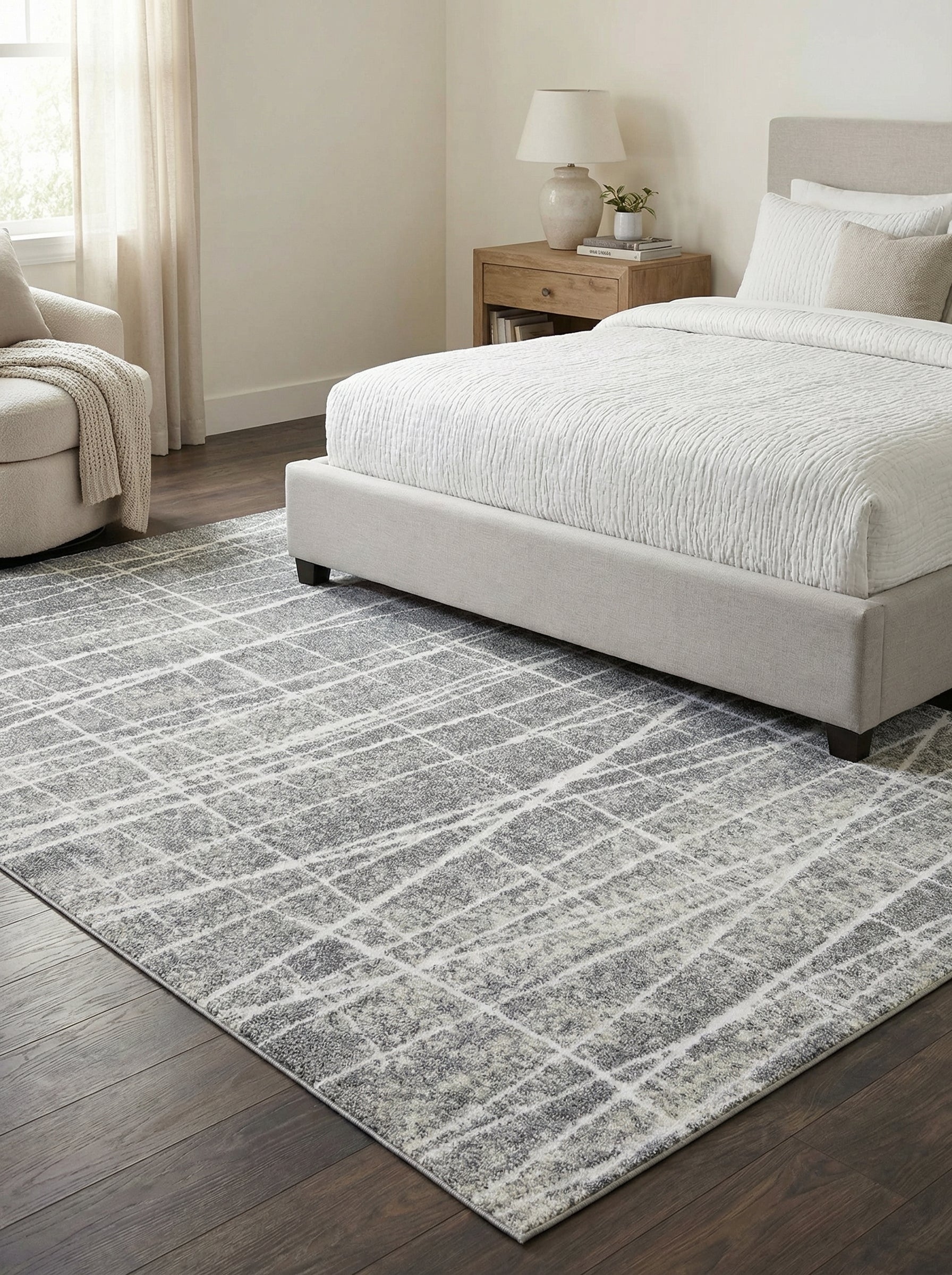 Tapis rectangulaire gris moucheté avec des lignes blanches croisées irrégulières, sur un parquet foncé dans une chambre