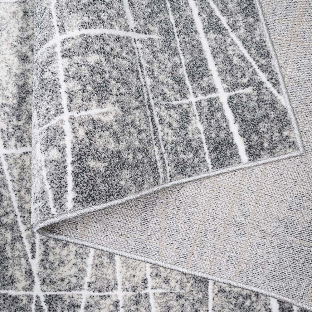 Tapis texturé aux tons gris et blanc avec un motif de lignes irrégulières formant une grille, le revers est également visible