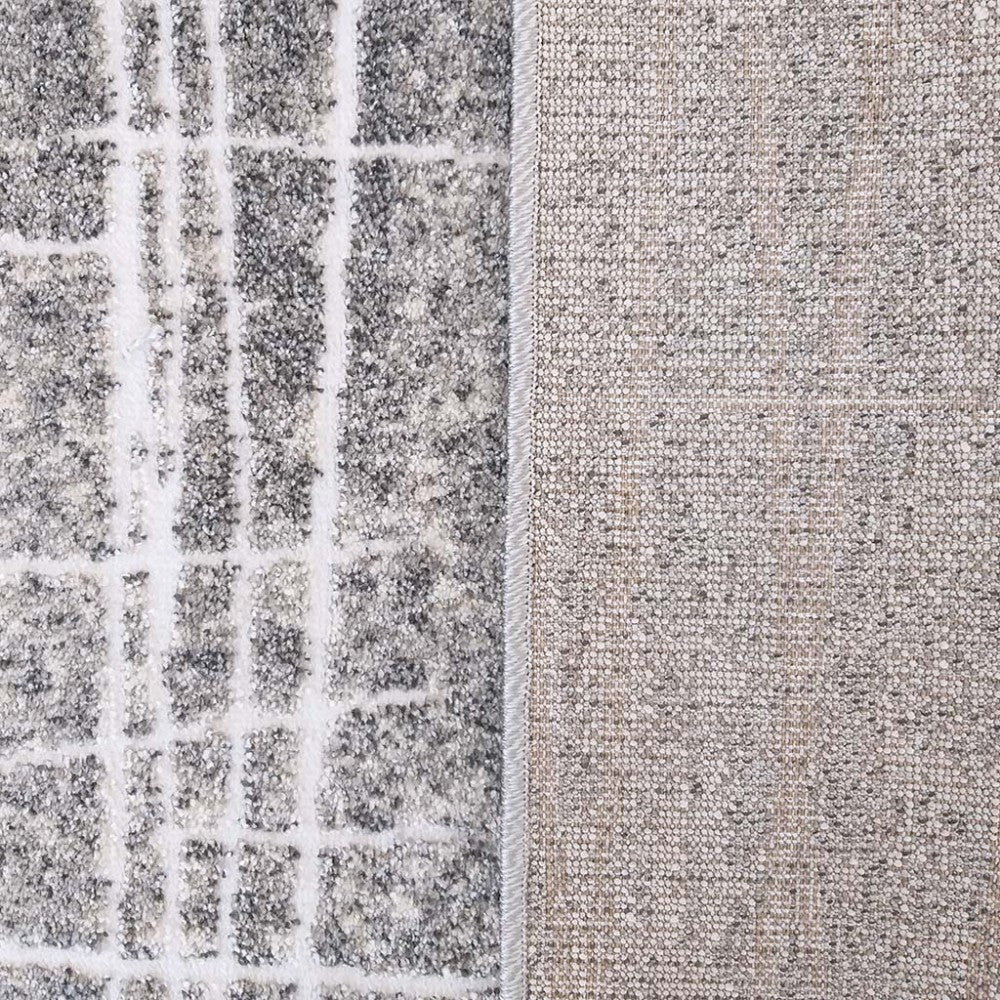 Tapis présentant sa face visible à motifs de lignes blanches irrégulières sur fond gris chiné et son dos tissé beige