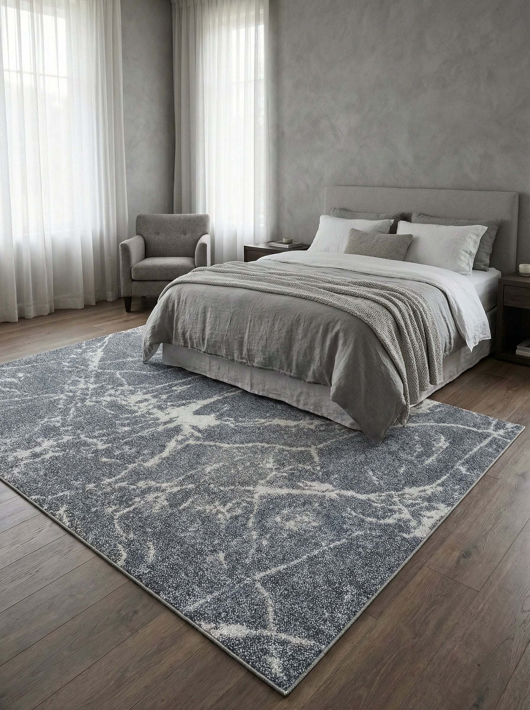 Tapis rectangulaire gris foncé moucheté de blanc aux motifs abstraits et irréguliers, posé sur un plancher en bois dans une chambre