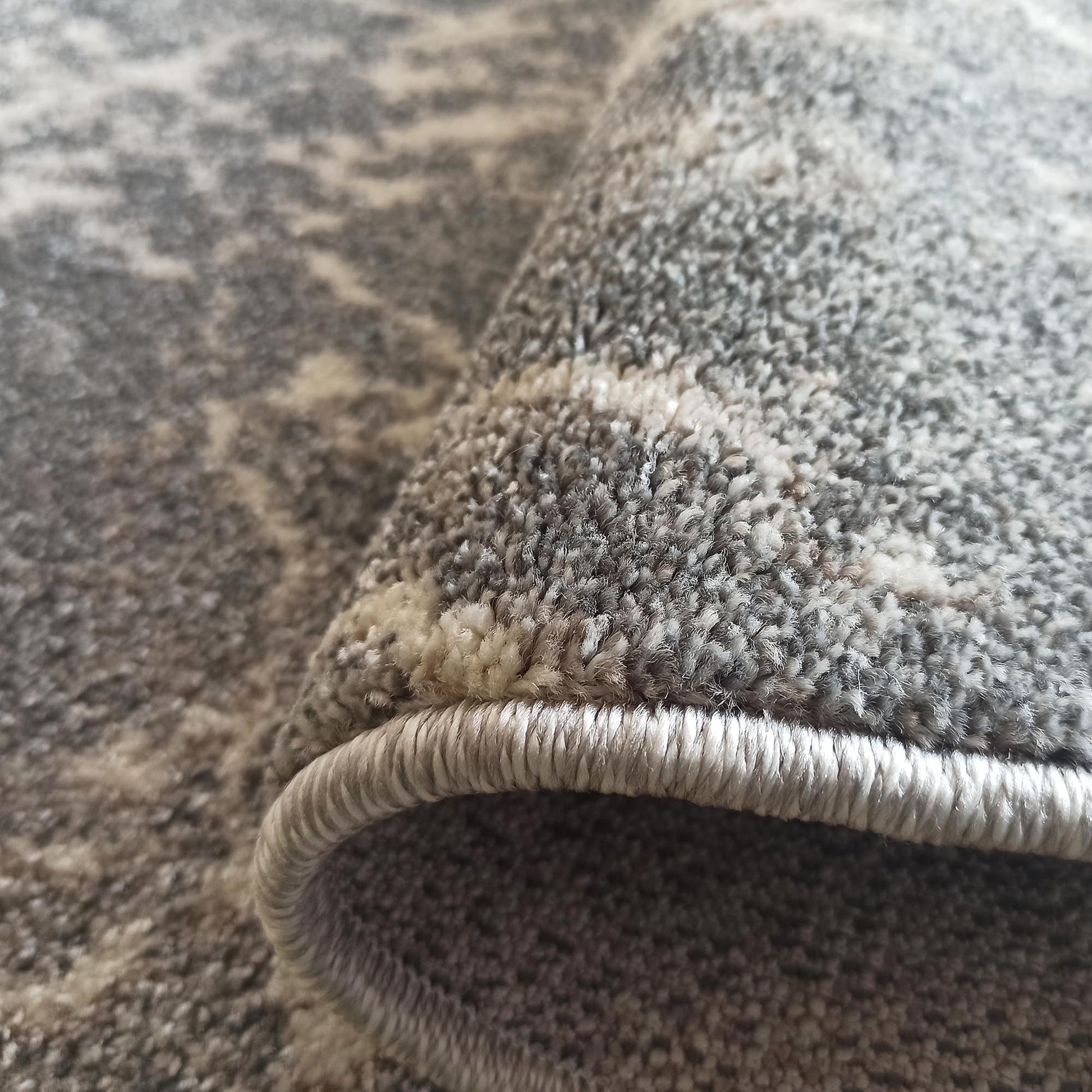 Gros plan sur un tapis texturé aux motifs abstraits gris et crème, avec un bord surpiqué