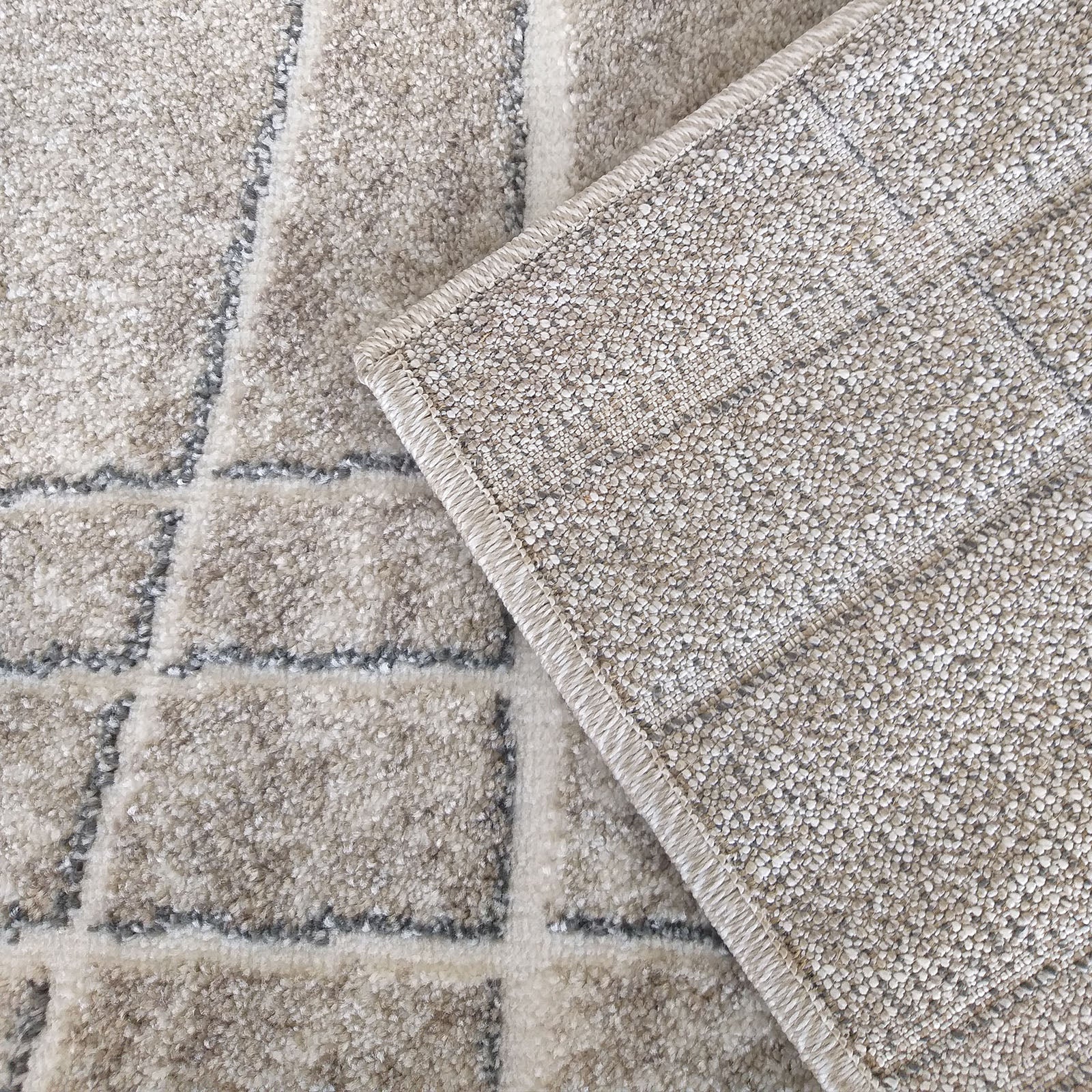 Tapis beige à surface texturée et motif quadrillé de lignes grises. Un coin est relevé, dévoilant l'envers granuleux du tapis